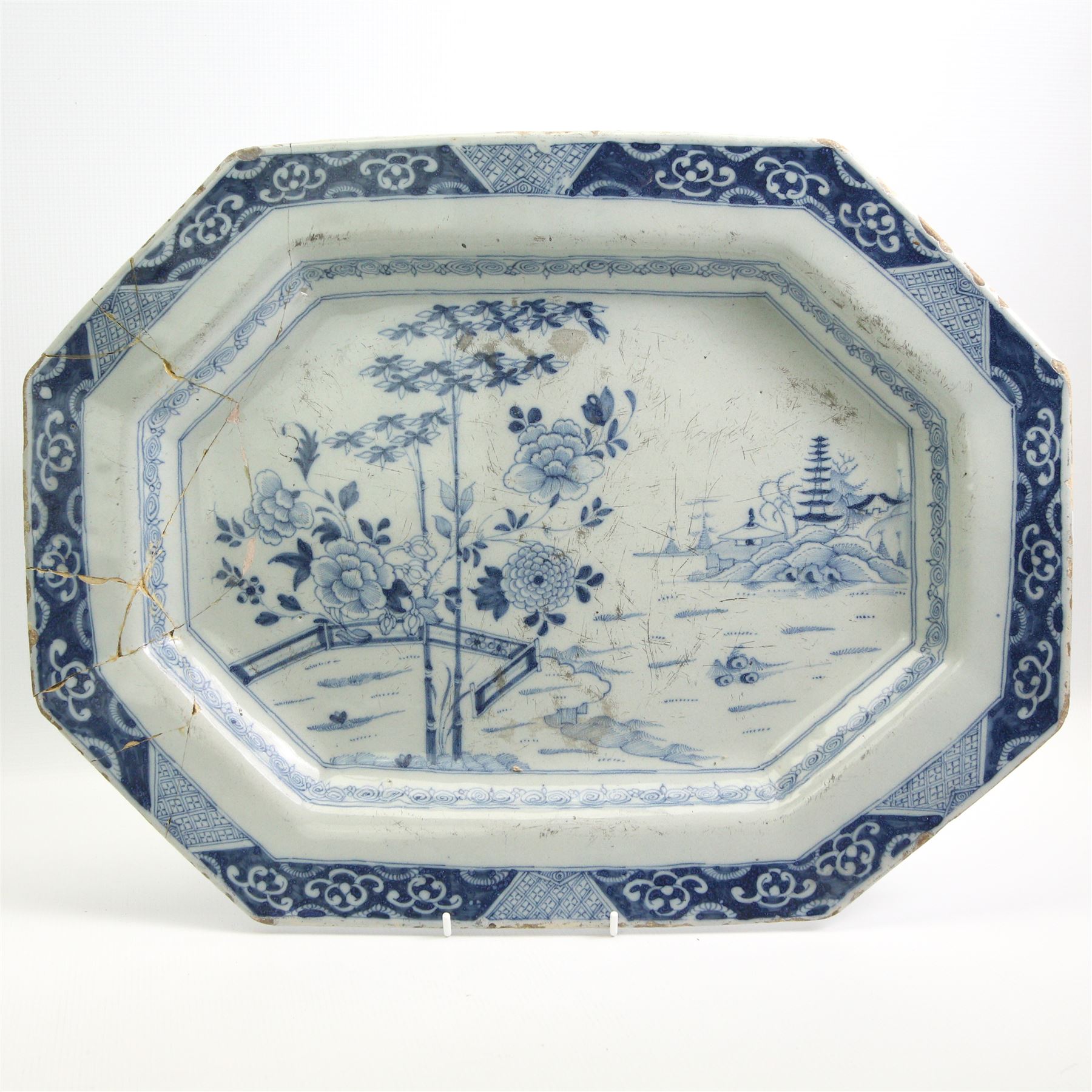 Two English Delft dishes, of canted rectangular form, painted with a fence, flowering plants and bamboo, within a scroll border, one marked F beneath, 49.5cm x 37.5cm max (2)