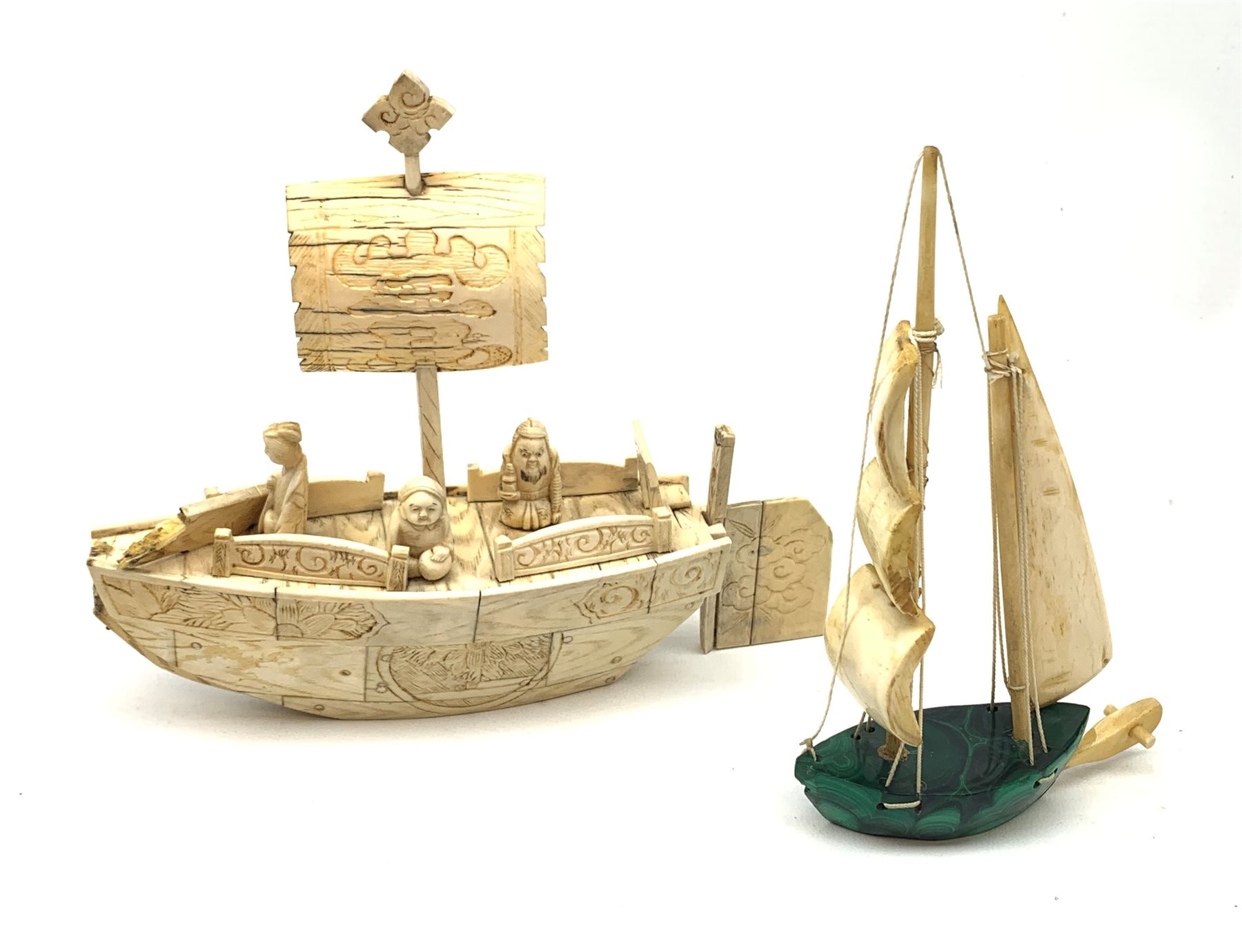 A Japanese carved ivory model of a sailing boat, surmounted by three carved figures (a/f), L22.5cm, together with a smaller sail boat with malachite hull and ivory sails and rudder, H18cm. 