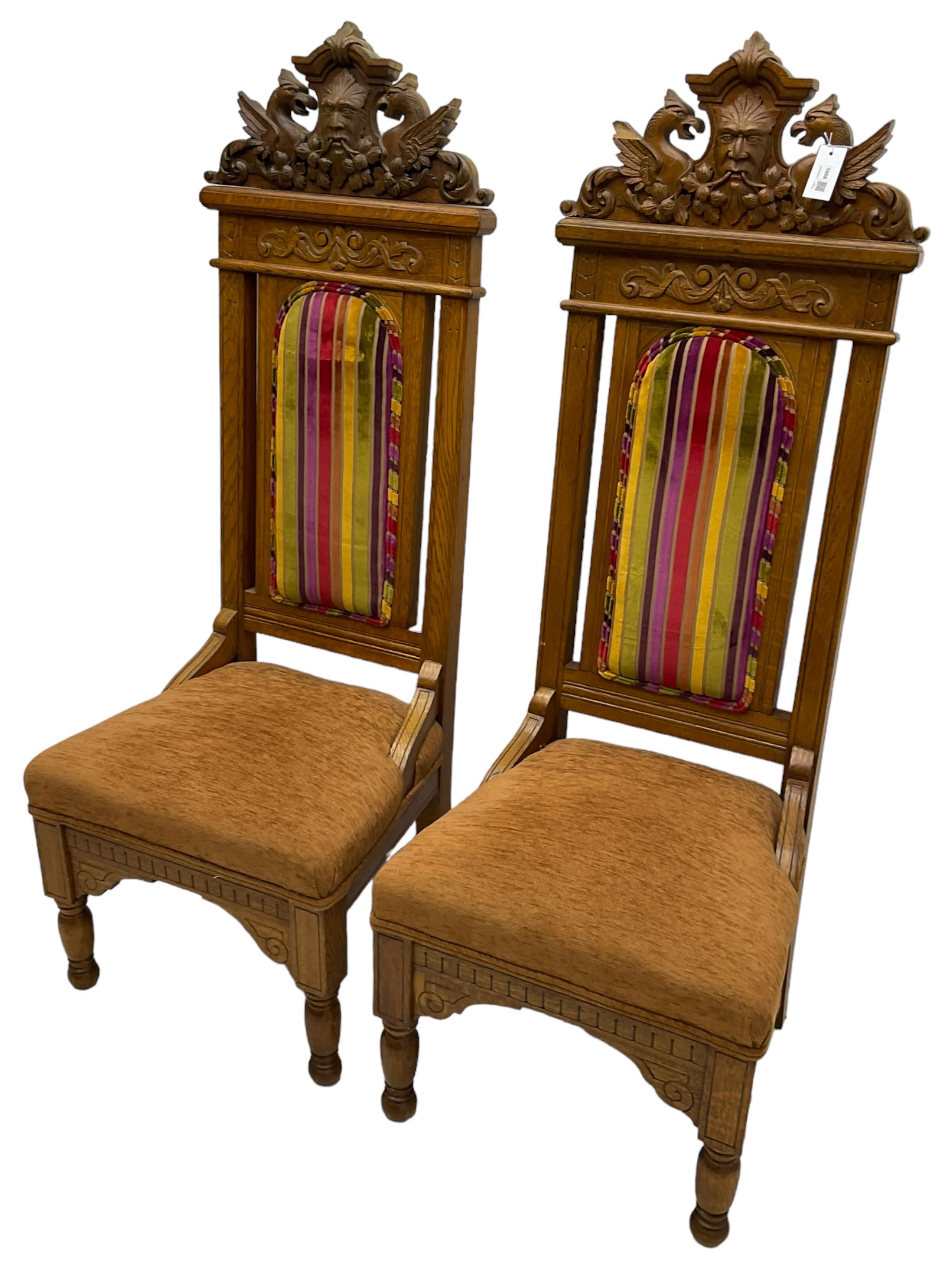 Set of six 20th century Carolean design oak high back chairs, the pediment carved with dragons and central Green Man mask with trailing foliage, the backs upholstered in striped fabric, on turned front supports