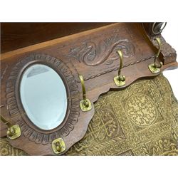 Late 20th century oak wall hanging coat rack, central bevelled oval mirror in foliate carved surround, decorated with S-scrolls and lion masks, fitted with needlework hanging 