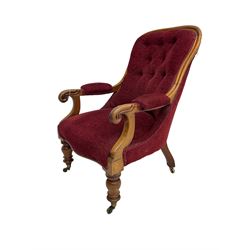 Victorian mahogany framed open armchair, upholstered in buttoned red fabric, the arm terminals carved with scrolls, on turned front supports with brass cups and castors