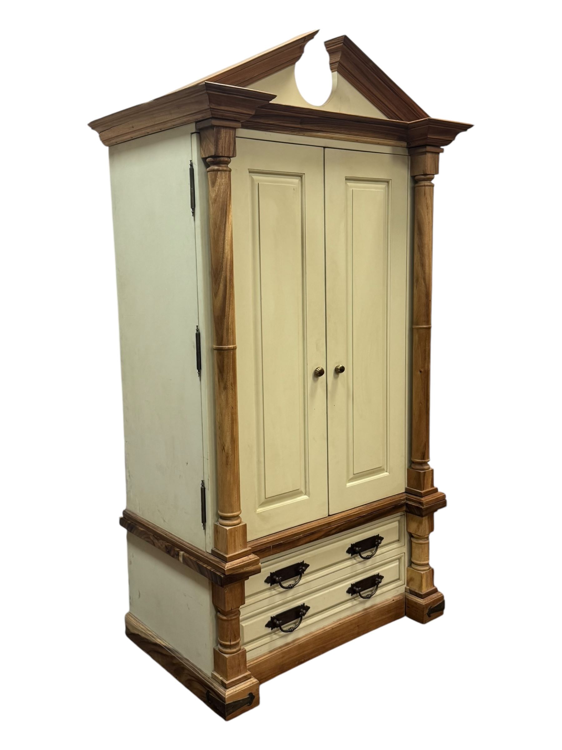 Hardwood and cream painted kitchen larder cupboard, sloped pediment over two panelled doors, the interior fitted with slides, drawers and storage shelves, two long drawers below, mounted by turned pilasters, on metal bound moulded plinth base