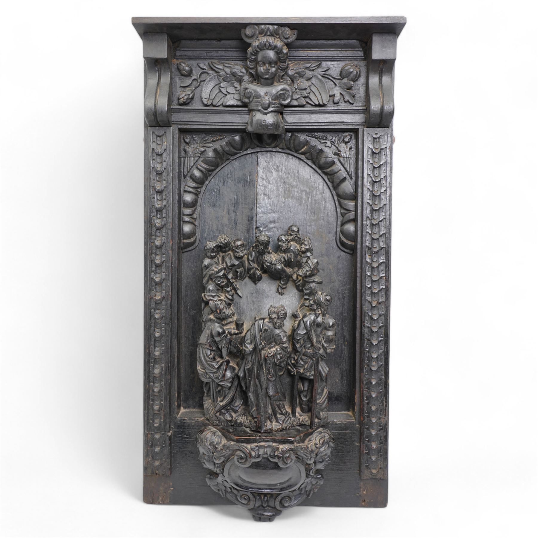 Late 17th century South German or Flemish carved oak figural group depicting 'The Last Supper', comprised of twelve figures facing each other around a central table, standing on on a later oak panel, the frieze carved with a central female mask flanked by foliate carvings, the group presented under an egg-and-dart carved arch, the base decorated with a protruding cartouche, flanked by cherub masks