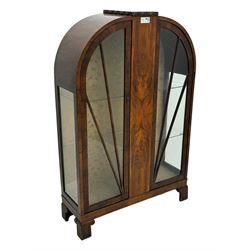 Early 20th century Art Deco walnut display cabinet, with arched top and carved floral crest, central band flanked by two glazed panel doors with decorative mullions, enclosing two glass shelves, on scroll carved bracket feet