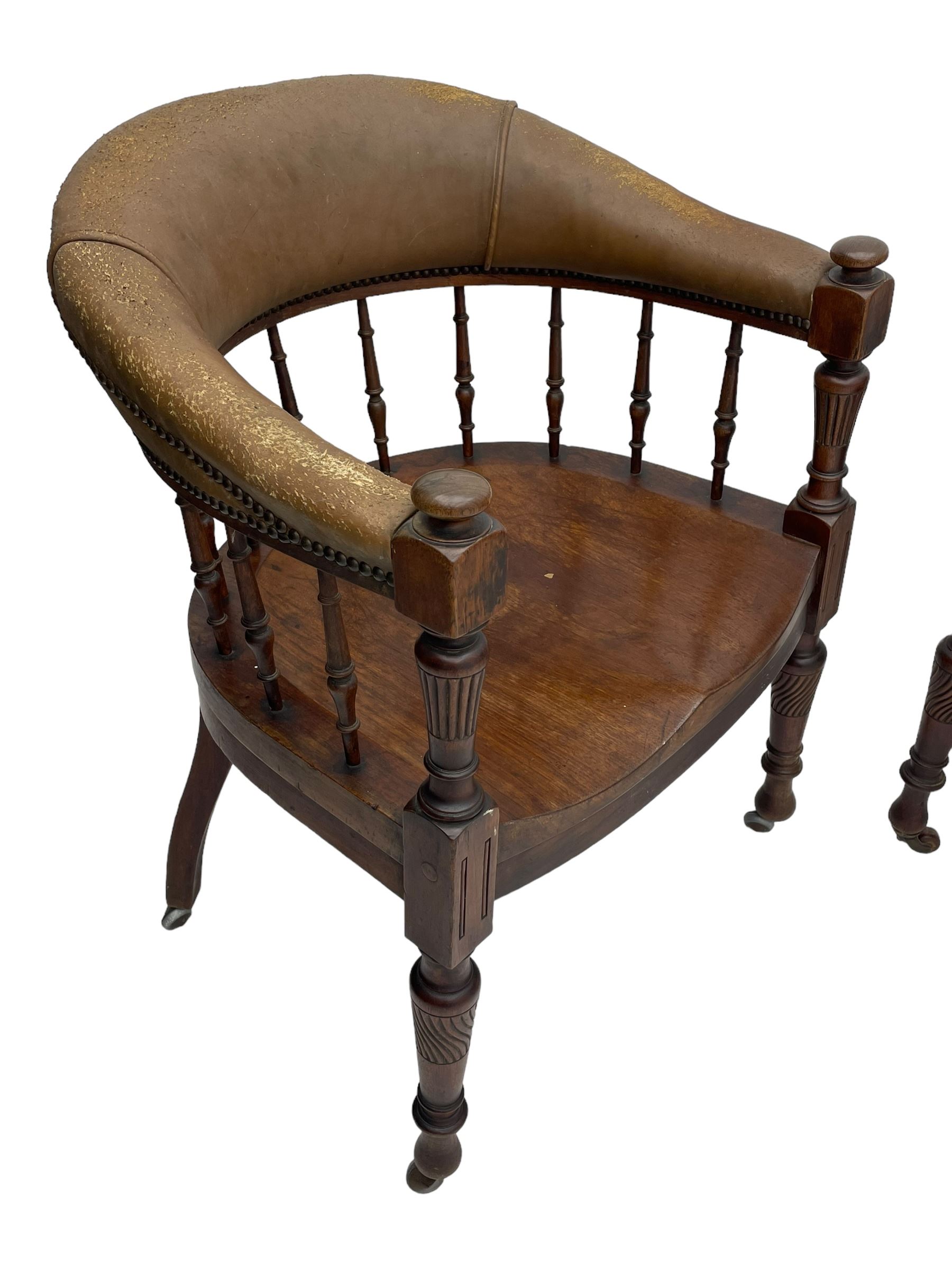 Pair of late Victorian walnut tub-shaped elbow chairs, the cushioned cresting rail upholstered in leather on spindle turned supports, dished saddle seat on turned supports