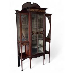 Art Nouveau period inlaid mahogany display cabinet, raised shaped and moulded pediment over projecting moulded cornices, the upper frieze inlaid with trailing branches and tulips, single astragal and bevel glazed door enclosed velvet lined interior fitted with shelves, flanked by curved glass panes decorated with pierced metal foliate spandrels, lower flanking shelves with mirror backs enclosed within shaped and pierced rails inlaid with flower heads, on tapering octagonal supports terminating to compressed pad feet, the lock stamped 'Salmon Bros, London' 