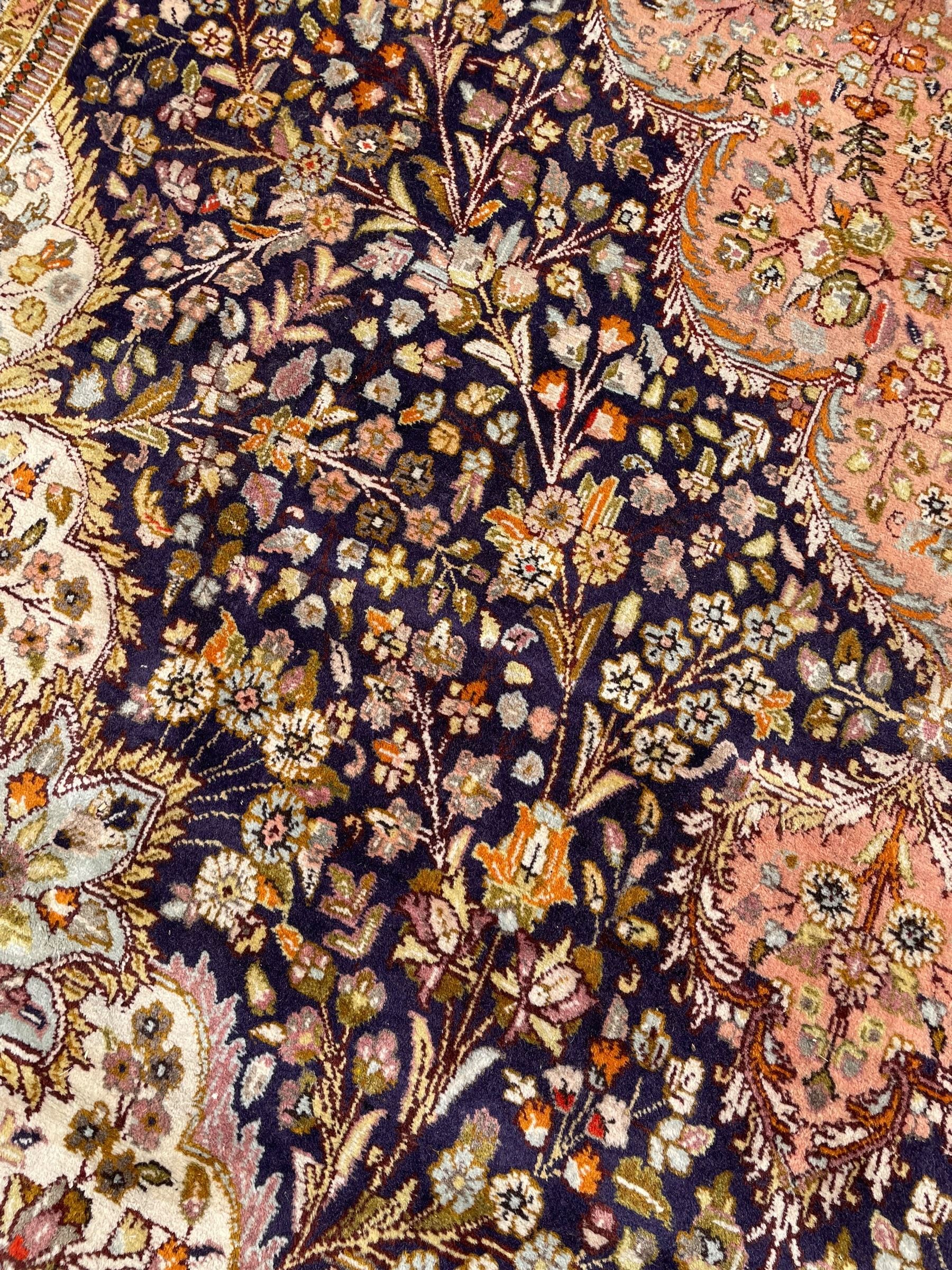 Persian Kashan, scalloped central medallion on indigo ground field, decorated profusely with branch shoots with floral motifs, pale ground spandrels decorated with stylised flower head motifs, crimson ground border decorated with repeating palmettes and trailing leafy branches, within multiple guard stripes 