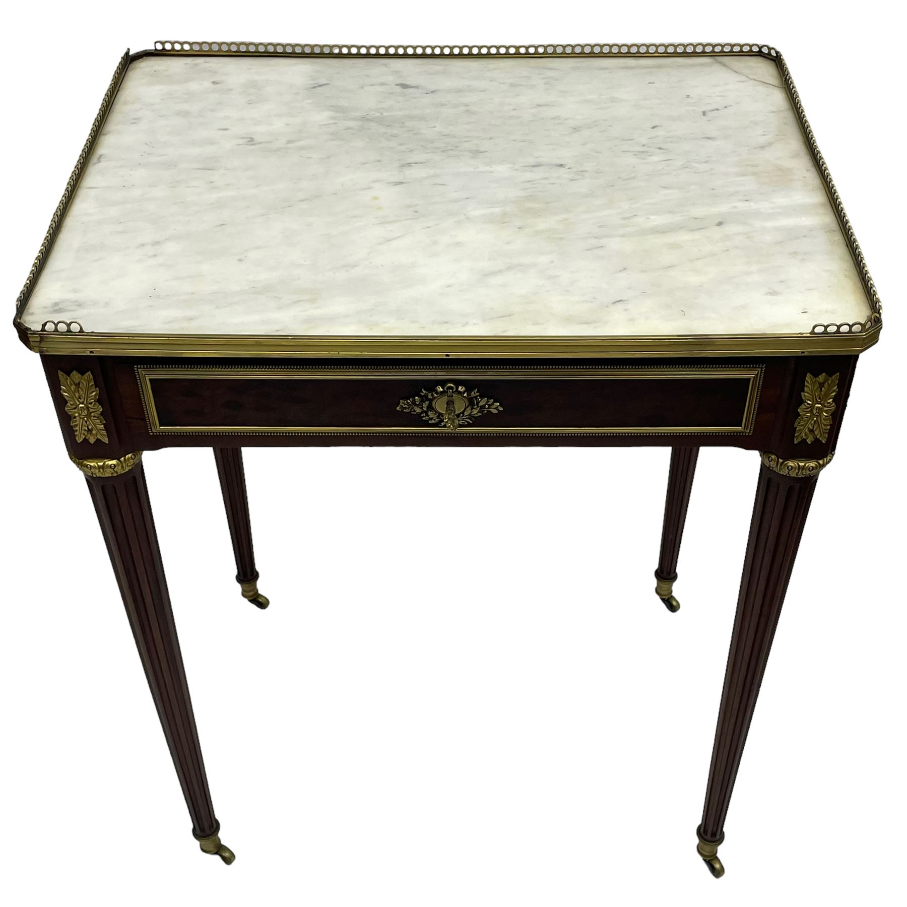 Late 19th century French figured plum pudding mahogany side table, canted rectangular white marble top with raised gilt metal gallery, fitted with a single frieze drawer, central extending floral cast ormolu escutcheon and applied moulded edging, on tapering turned and fluted supports with brass cups and castors, decorated with cast foliate mounts and foliate cast collars 