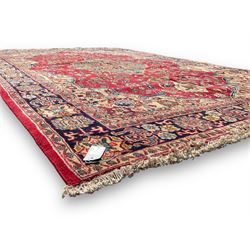 Central Persian Isfahan crimson ground carpet, central floral medallion in ivory and blue, set within a field of dense floral patterns, bordered by a navy band decorated with stylised flower heads and vines