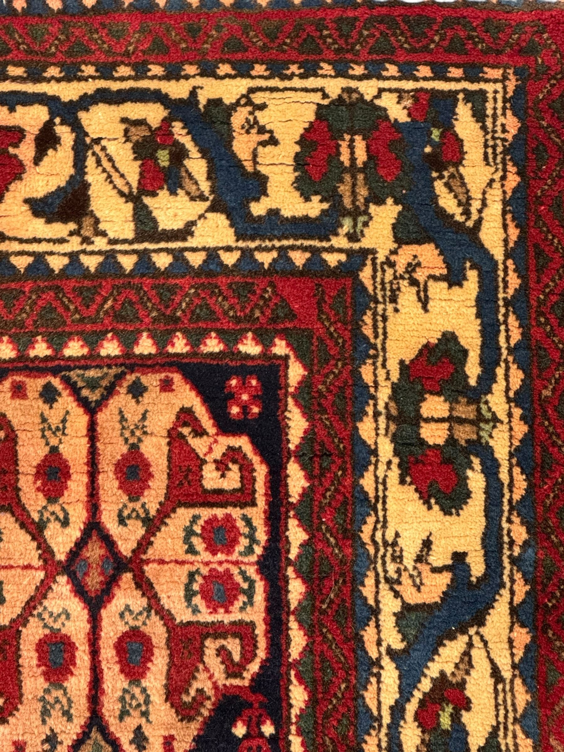 South West Persian Abadeh crimson ground rug, indigo ground with crimson lozenge field, decorated all over with small stylised motifs of flowerheads, hooks, animals and birds, guarded border decorated with trailing leaves and stylised plant motifs 