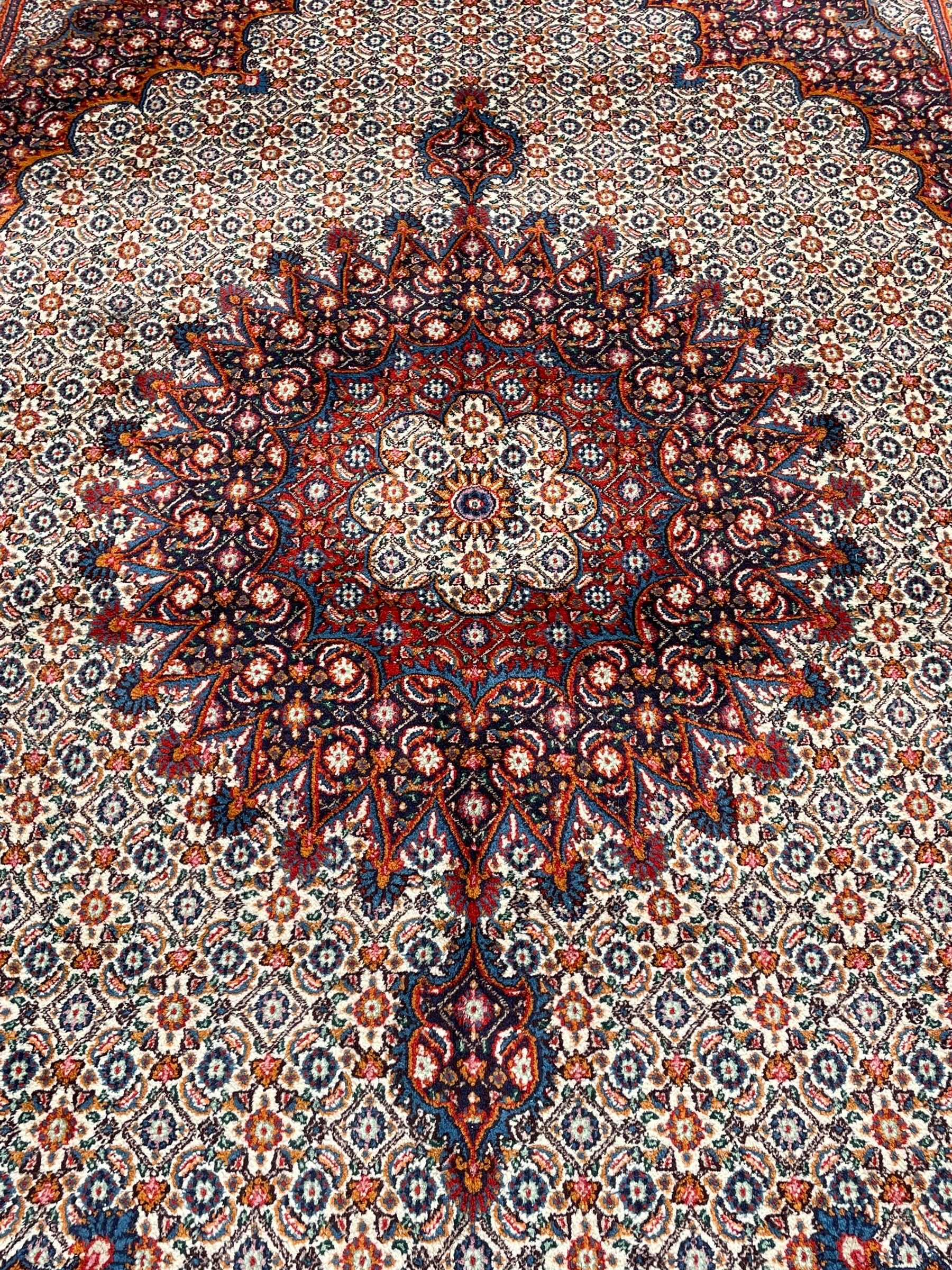 Persian Bidjar ivory and indigo ground rug, large central rosette medallion surrounded by floral herati motifs, crimson ground border decorated with repeating palmettes, within guard stripes decorated with small flower head motifs 