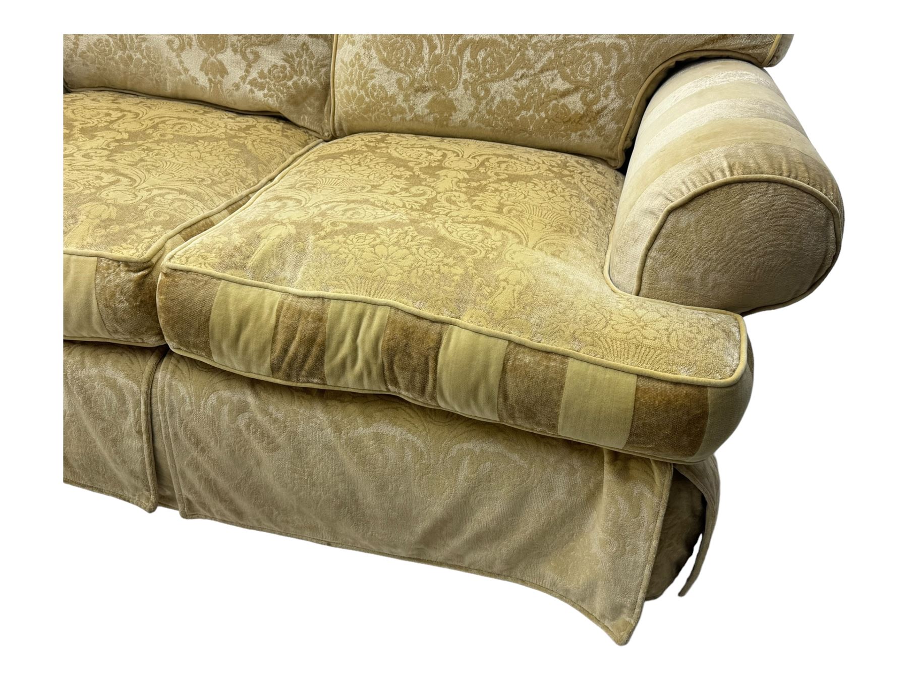 Contemporary two-seat sofa, upholstered in damask fabric with a pale gold floral pattern, rolled arms, loose back and seat cushions, on matching skirted base with concealed castors