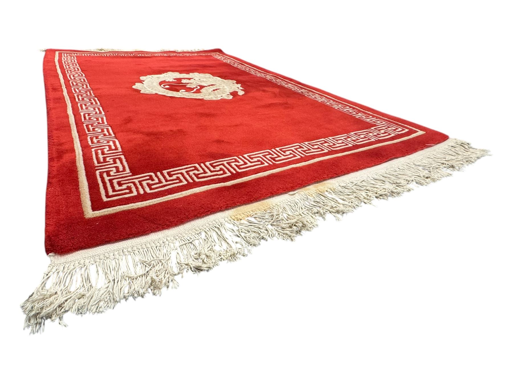 Chinese washed woolen red ground rug, central circular dragon motif in ivory, framed by a decorative Greek key border in matching ivory tones, finished with fringed ends