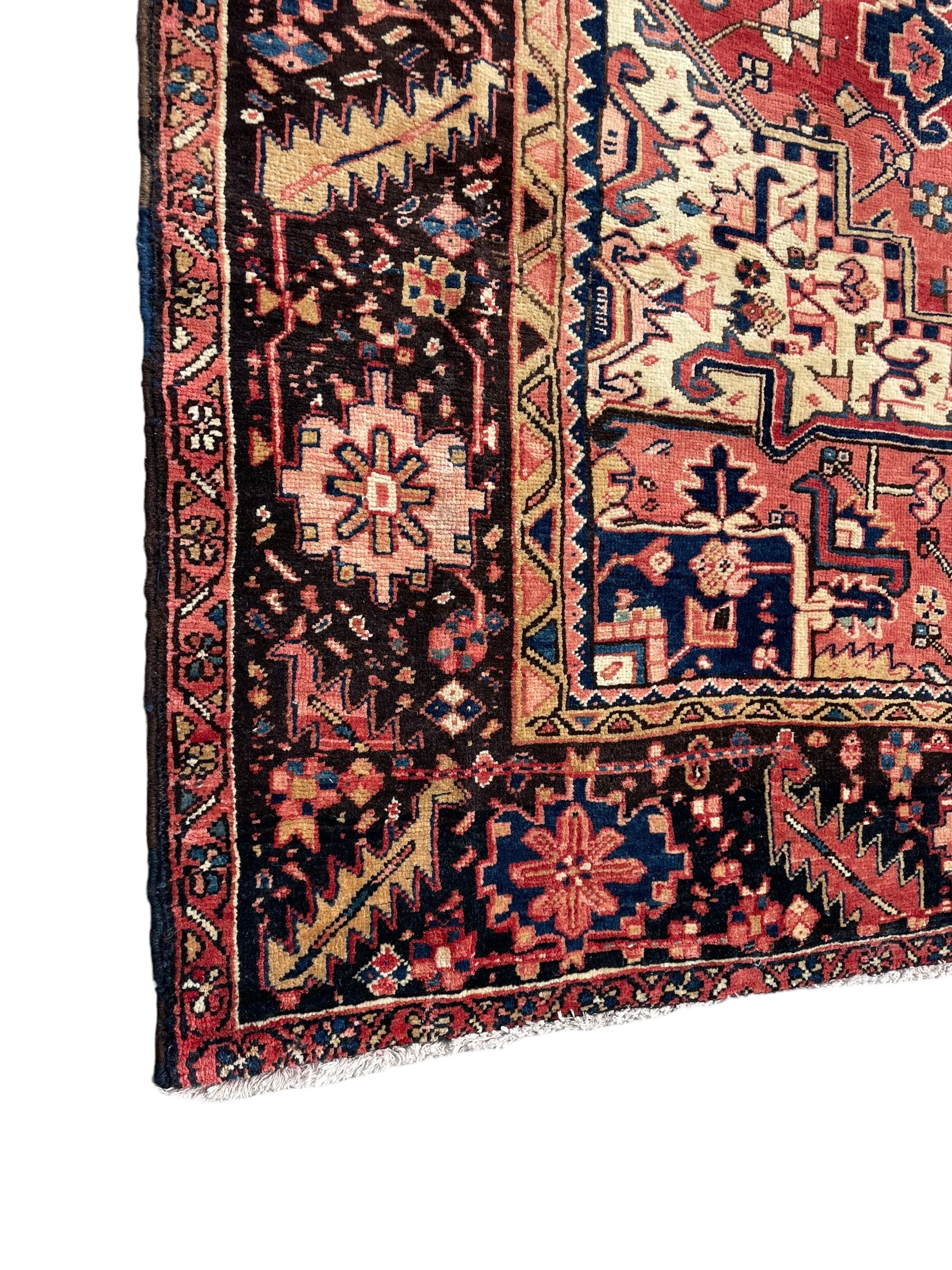 Persian Heriz red ground carpet, large central eight point medallion with projecting palmettes surrounded by small geometric motifs, decorated profusely with hooks, rosettes and animals, the busy border decorated with stylised foliate motifs within guard stripes 