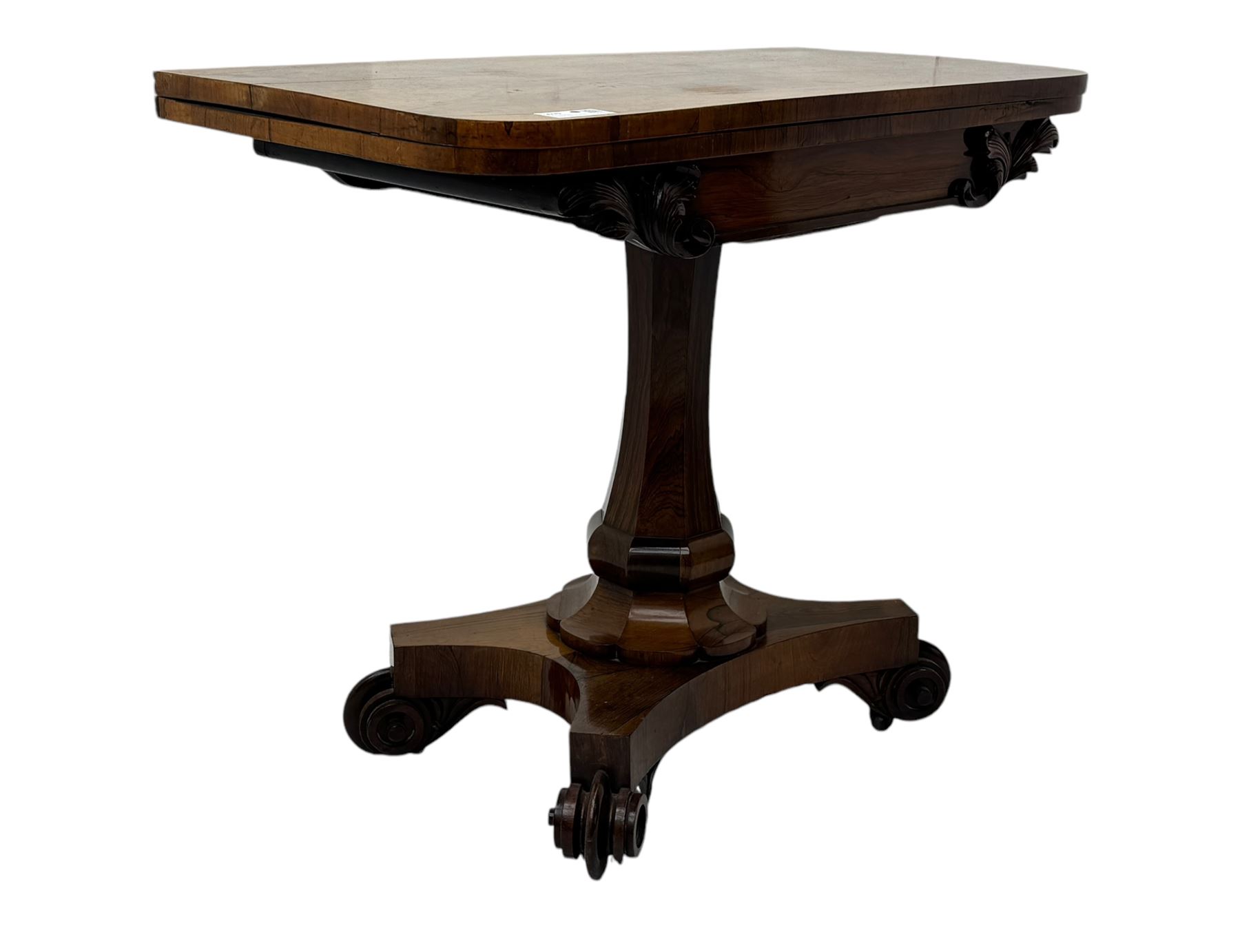 Early Victorian rosewood card table, rectangular foldover swivel top with rounded corners, red baize-lined surface, frieze adorned with carved foliate motifs, supported by a central octagonal waisted column on shaped quatrefoil base, terminating in scrolled feet with concealed metal castors