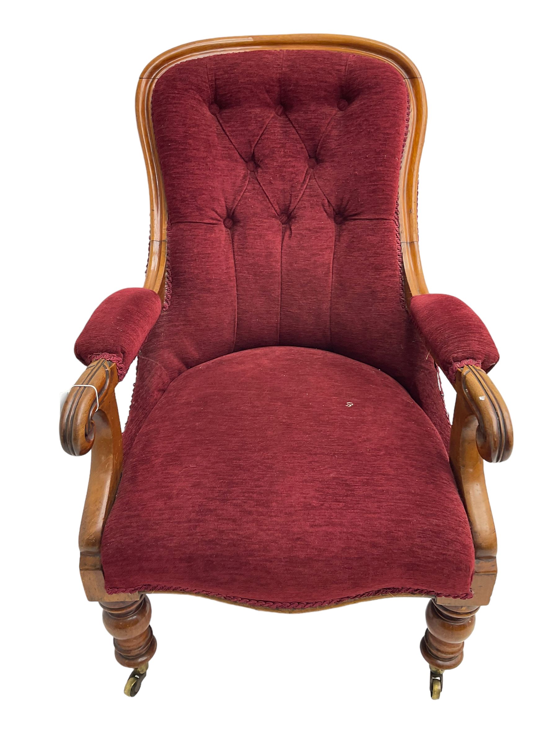 Victorian mahogany framed open armchair, upholstered in buttoned red fabric, the arm terminals carved with scrolls, on turned front supports with brass cups and castors