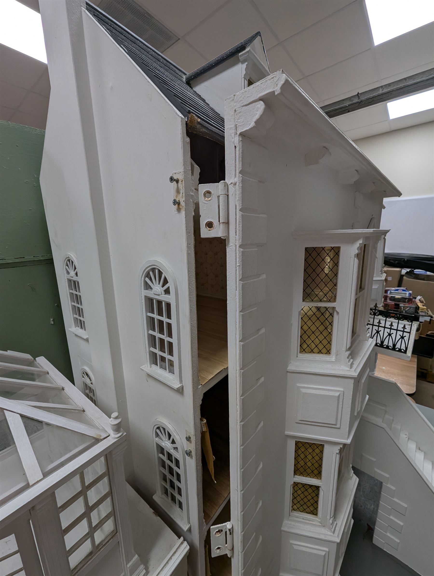 Large three storey modern dolls house, painted white with latticed windows, grey roof and metal fencing, with decorated interior, together with two dolls house garden rooms and two conservatories