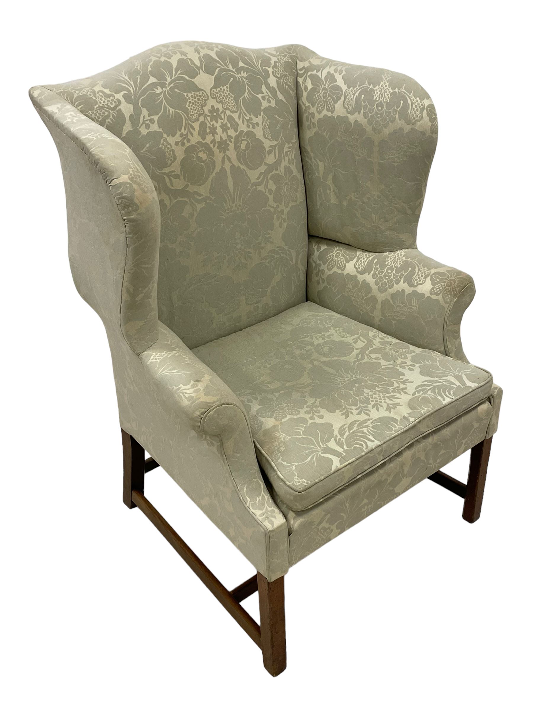 Georgian mahogany framed wingback armchair, upholstered in floral pattern silk damask fabric, wide seat enclosed by rolled arms, on chamfered square supports united by plain stretchers 