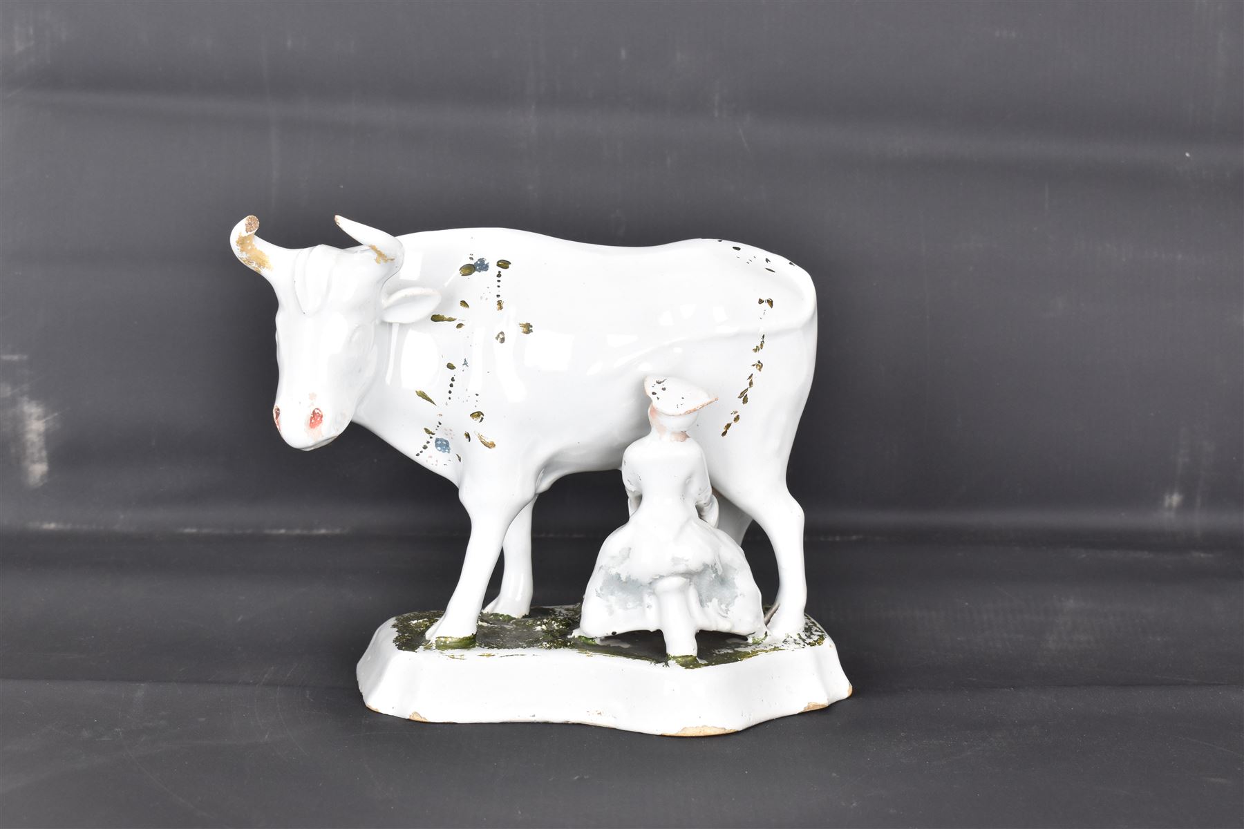 19th century Delft figure group depicting a milkmaid milking a cow, H17.7cm