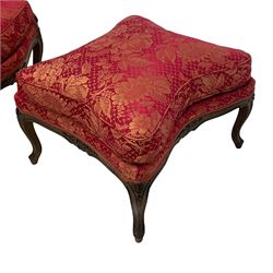 Late 20th century French design stained beech framed armchair and matching stool - the armchair with shaped and moulded frame carved with flower heads and foliage, upholstered in silk red and gold ground fabric with floral pattern, on scroll carved cabriole feet decorated with flower head carvings (W73cm, H82cm, D75cm); the footstool of concaved rectangular form with moulded frame carved with flower heads, upholstered loose cushion, on cabriole feet (70cm x 64cm, H48cm)