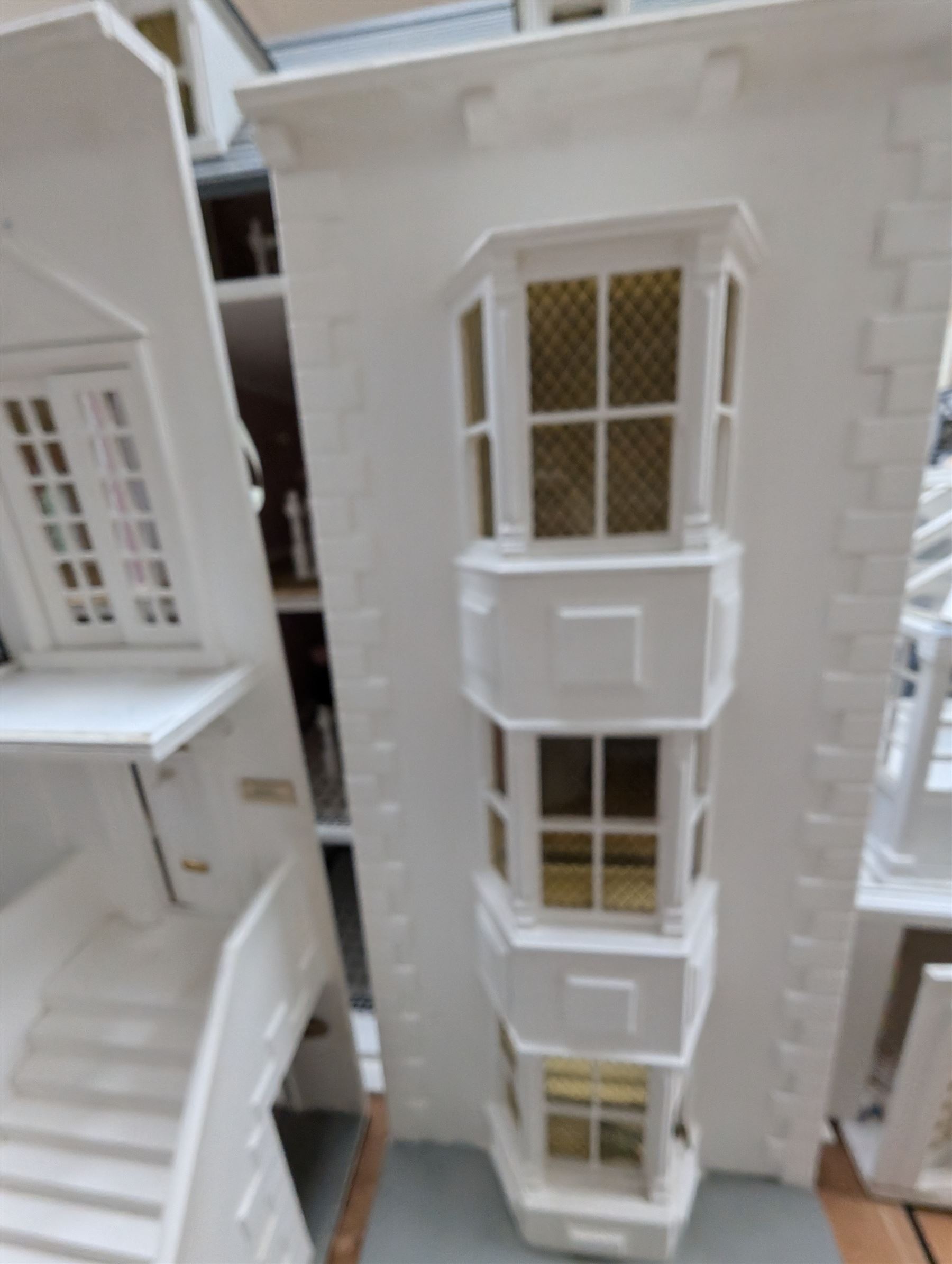 Large three storey modern dolls house, painted white with latticed windows, grey roof and metal fencing, with decorated interior, together with two dolls house garden rooms and two conservatories