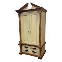 Hardwood and cream painted kitchen larder cupboard, sloped pediment over two panelled doors, the interior fitted with slides, drawers and storage shelves, two long drawers below, mounted by turned pilasters, on metal bound moulded plinth base