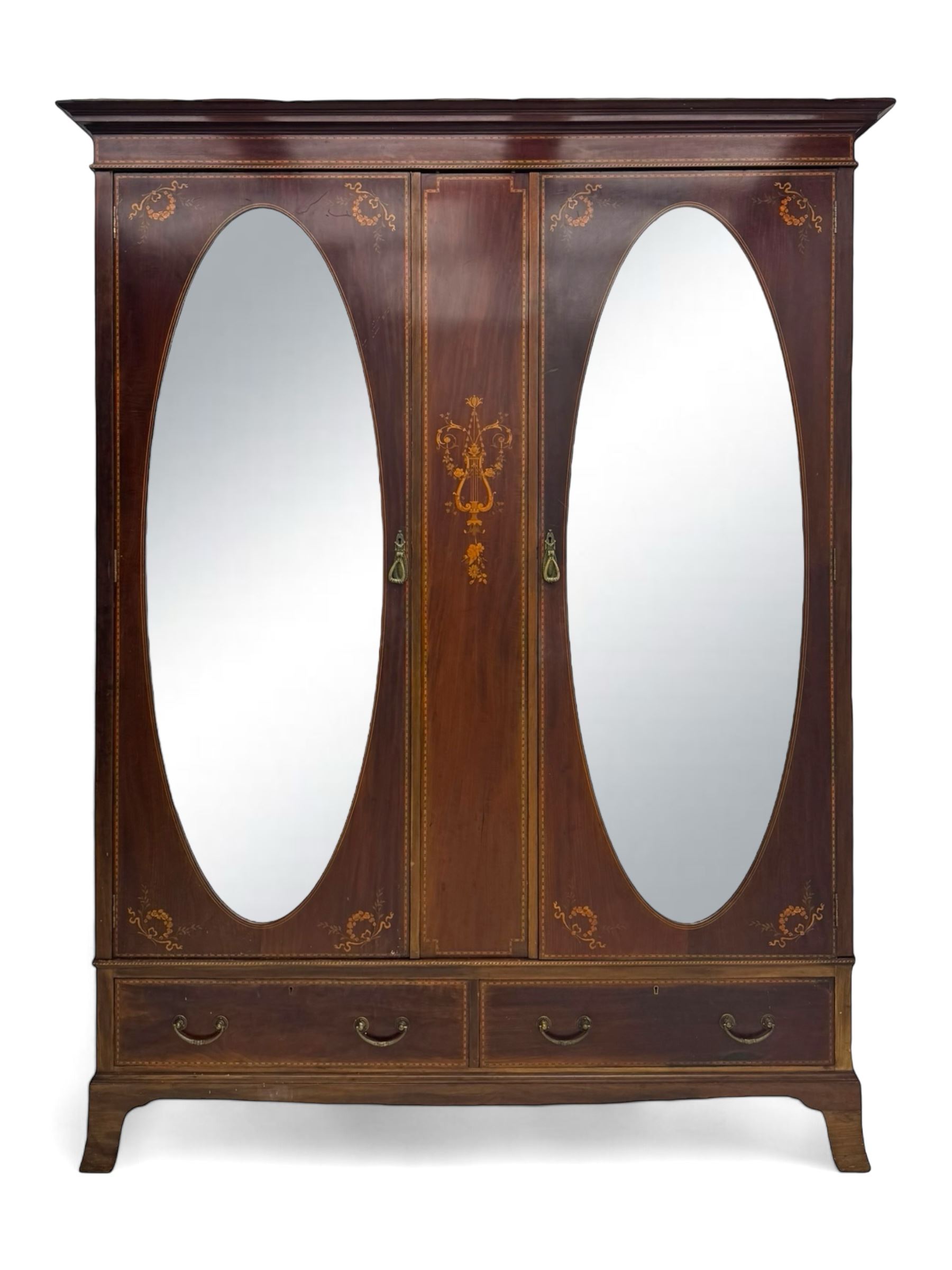 Maples & Co. - Edwardian mahogany wardrobe, projecting cornice over frieze inlaid with checkered stringing, central vertical panel inlaid with lyre and scrolling foliate decoration, two oval mirror glazed doors enclosing hanging rails and hooks, the base fitted with two short drawers, on splayed bracket feet