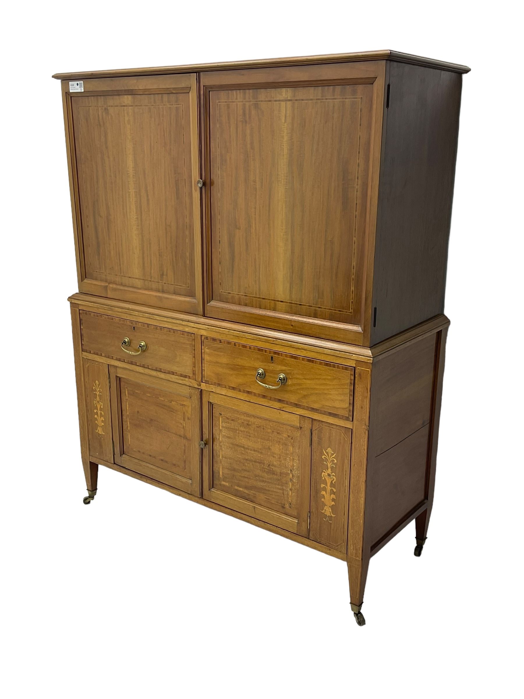 Early 20th century inlaid mahogany cabinet, two-door upper section revealing interior shelving and two large pull-out drawers, the lower section comprises two wide drawers flanked by inlaid floral motif panels above a double-door cupboard, supported by tapering legs with brass castors