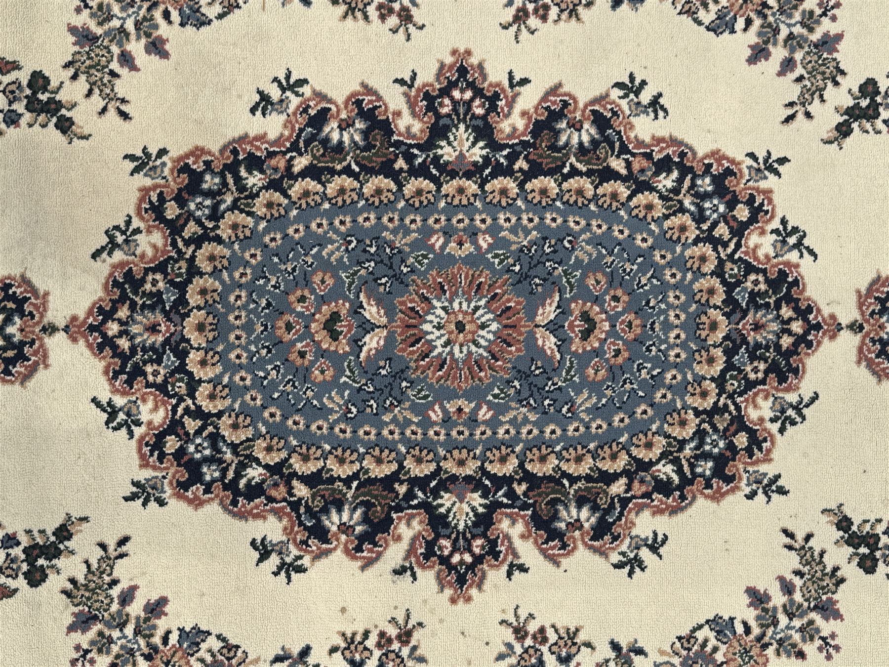 Persian design ivory ground rug, the field decorated with an oval medallion filled with floral motifs and scrolling vines, flanked by floral sprays and corner spandrels with palmette designs, the main border featuring a series of stylised floral patterns against a dark blue ground, enclosed by multiple guard stripes with geometric and floral motifs