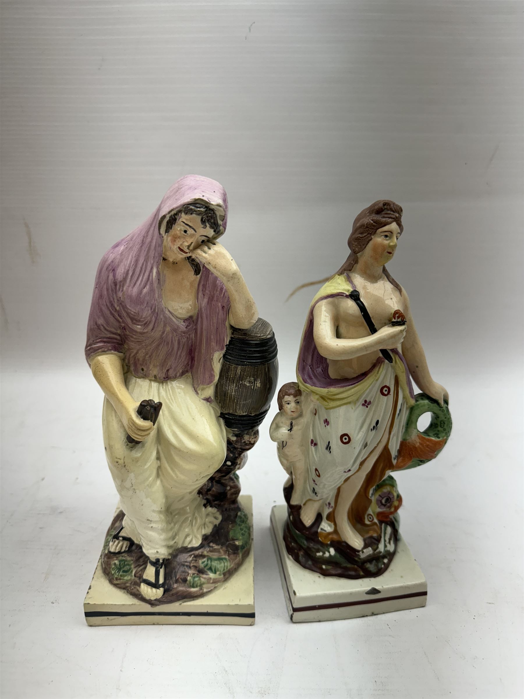 An early 19th Century Staffordshire pearlware figure of The Widow of Zarephath, H23cm, together with another pearlware example modelled as a classical figure in drapery, with putti by side, and supported by a zoomorphic fish to the other wise, H22cm