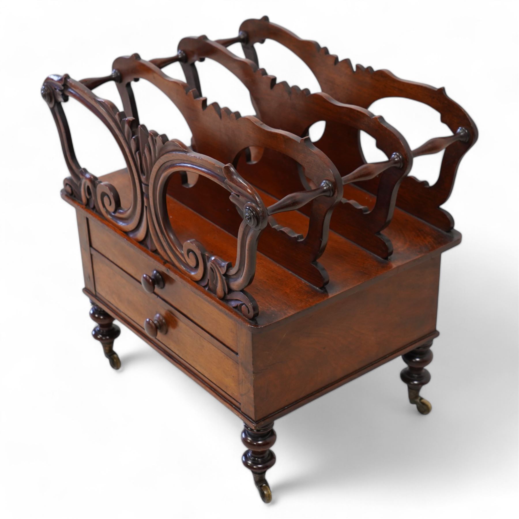 Victorian mahogany Canterbury, three divisions, carved with scrolls and curled leaf motifs, fitted with two drawers, on turned feet with brass cups and castors 