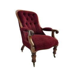 Victorian mahogany framed open armchair, upholstered in buttoned red fabric, the arm terminals carved with scrolls, on turned front supports with brass cups and castors