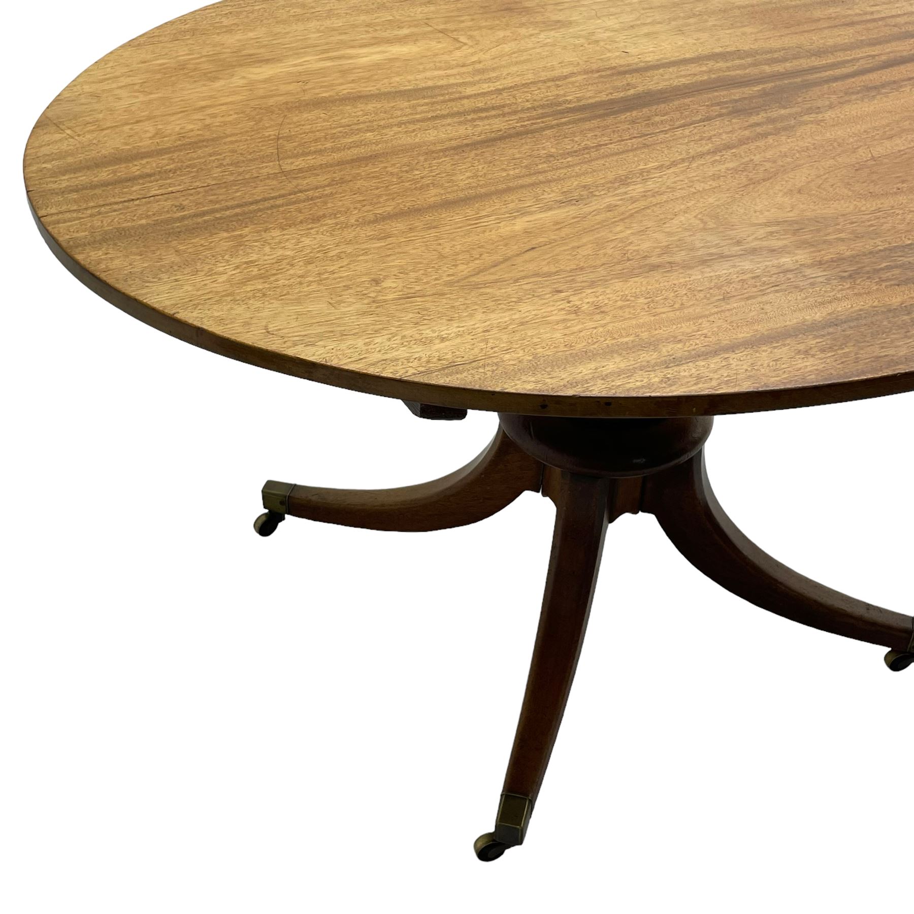 George III mahogany breakfast table, oval tilt-top on turned column with four splayed supports, fitted with brass cups and castors 