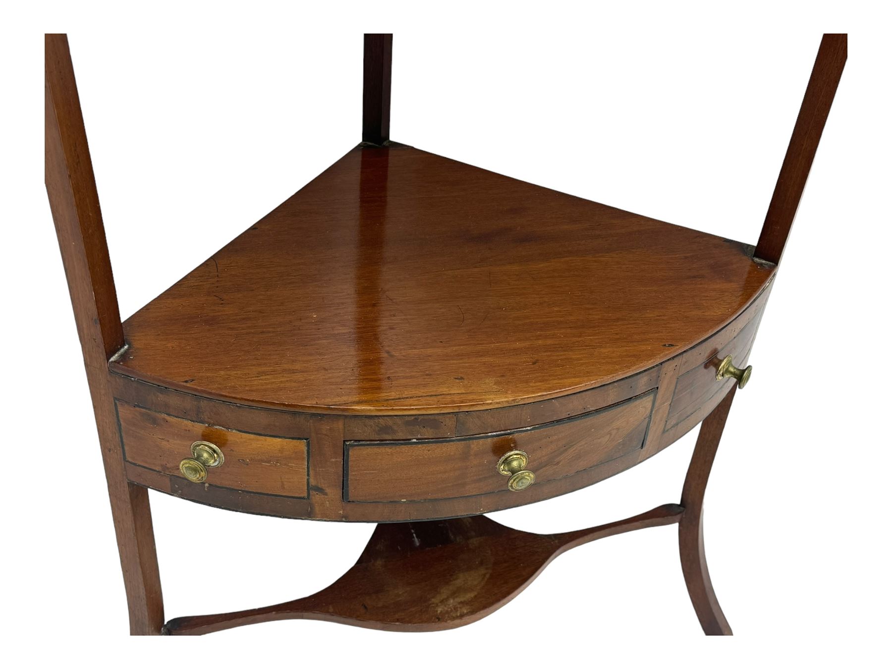 George III mahogany two-tier corner washstand, the inlaid top with geometric border, central drawer flanked by two faux drawers each with brass pull handle, on splayed supports united by shaped under-tier