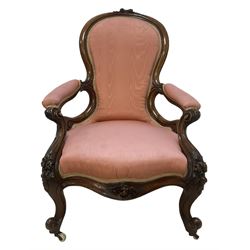 Victorian mahogany framed open armchair, spoon-back and sprung seat upholstered in pink fabric, scrolled arm terminals over serpentine fronted seat decorated with moulded carved floral motifs, cabriole supports with ceramic castors