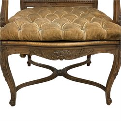 Late 19th century French carved beech open elbow chair, shaped cresting rail carved with central shell and curl leafage, cane work seat and back with buttoned loose seat cushion, the open arms carved with scrolled terminals and acanthus leaves, on cabriole supports with carved decorated united by shaped and moulded x-framed stretchers 