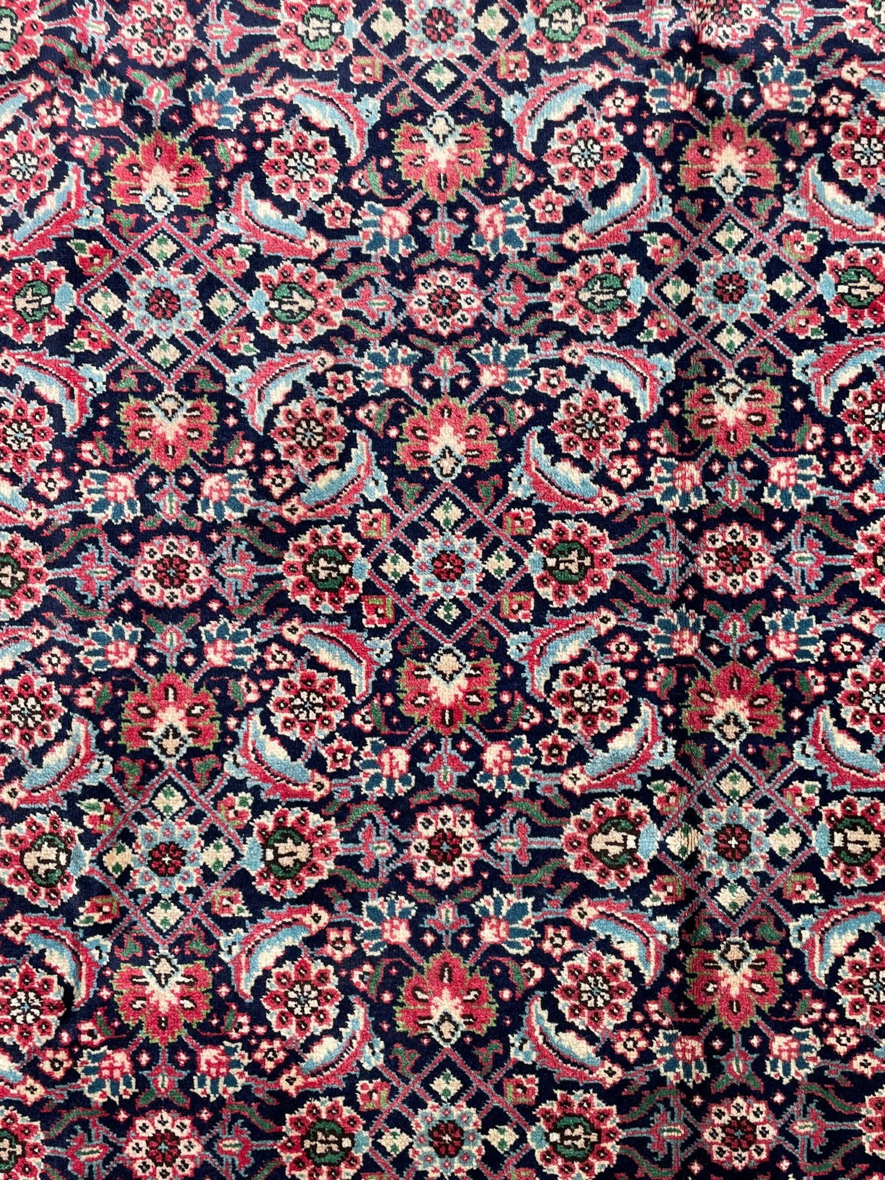 Persian Farahan indigo ground rug, the field decorated with large repeating floral herati motifs, crimson ground border decorated with palmettes and trailing leafy branch, within guard stripes 