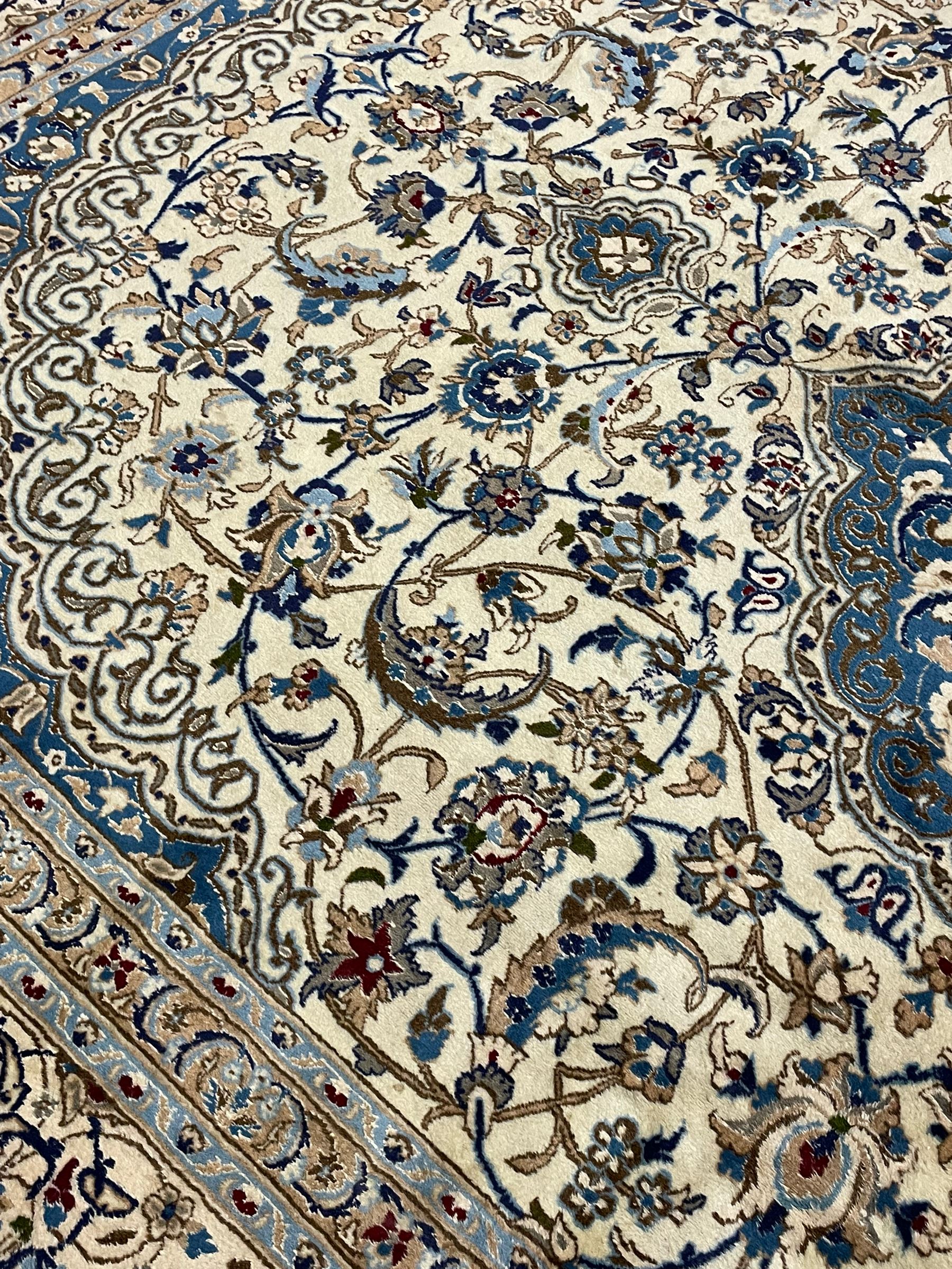 Persian Nain ivory ground carpet, the field decorated all over with leafy branches and stylised flower head motifs, blue ground central medallion and matching spandrels decorated with trailing foliate pattern, repeating guarded border with overall floral design