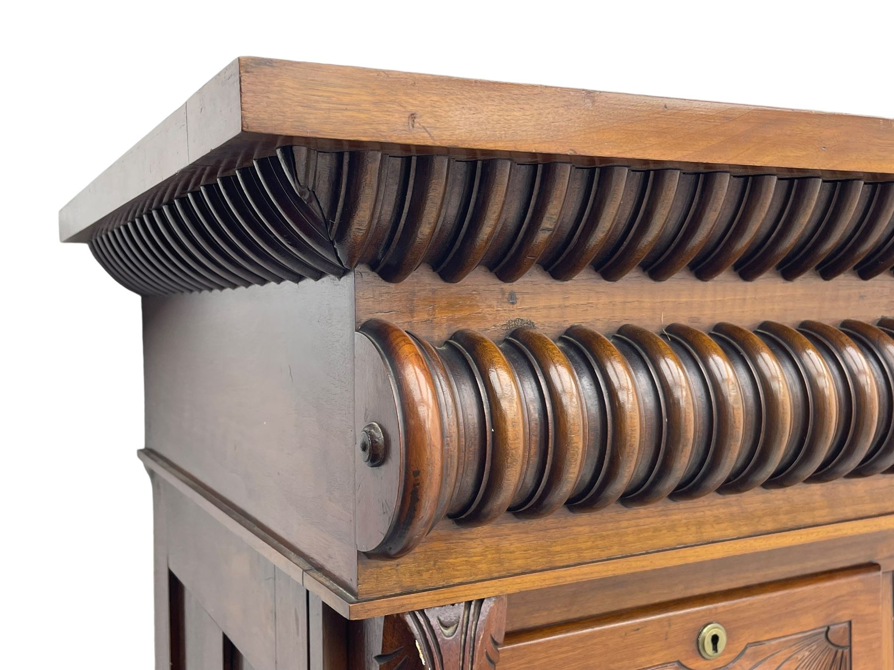 Late Victorian walnut Scotch chest, projecting cornice with turned quarter column mounts over matching half column to frieze, fitted with two upper short drawers with central cupboard, bevelled mirror glazed cupboard door, four graduating drawers below, foliage and flower head carved brackets to the uprights, panelled sides, chamfered plinth on turned feet