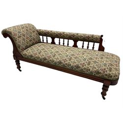 Late 19th century walnut framed chaise longue, upholstered in floral pattern fabric, rolled back rest and turned balustrade back, on turned feet with brass and ceramic castors 