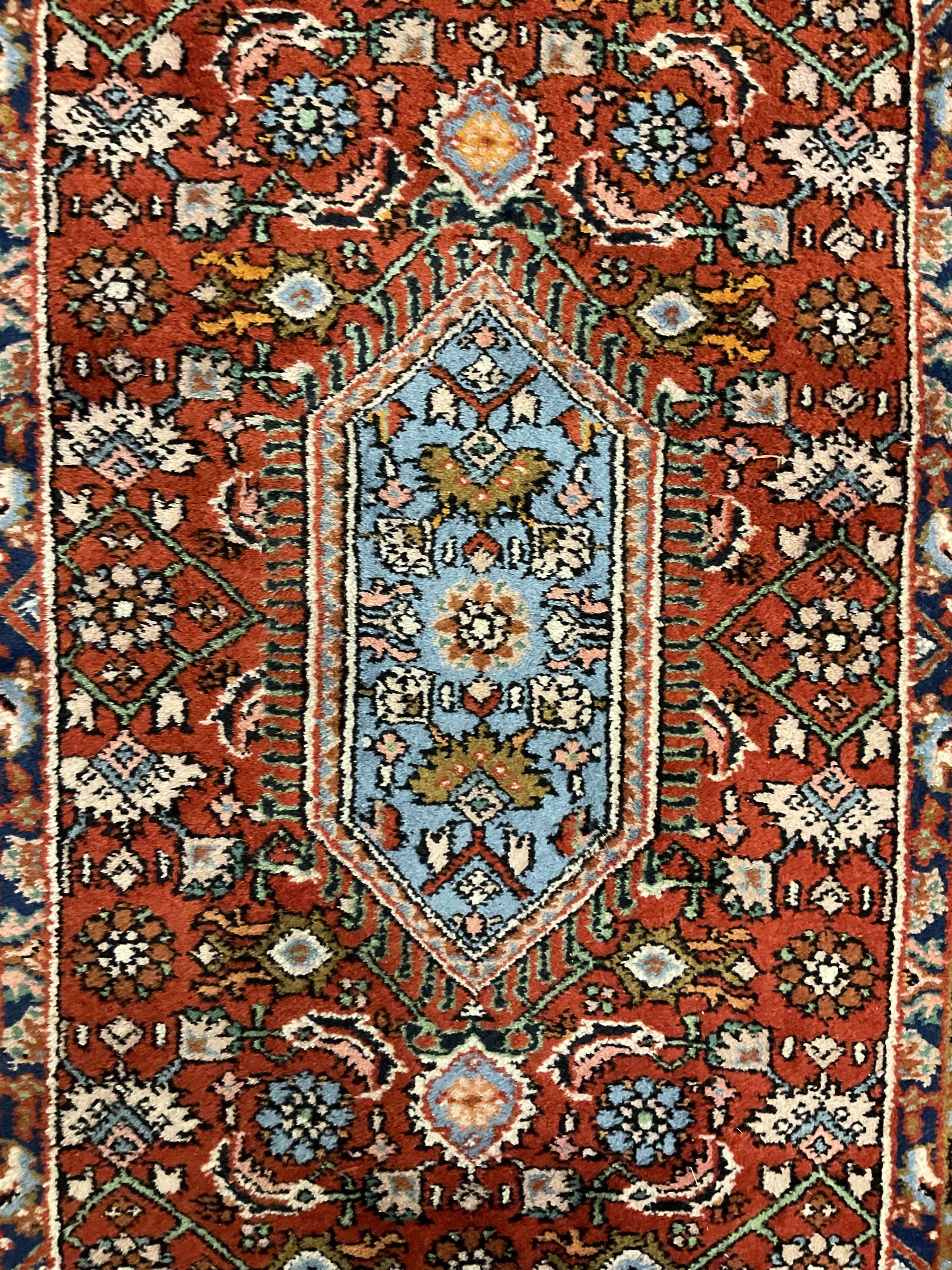 Small crimson ground rug, the extending lozenge field decorated with Herati motifs and flower heads, repeating guarded border