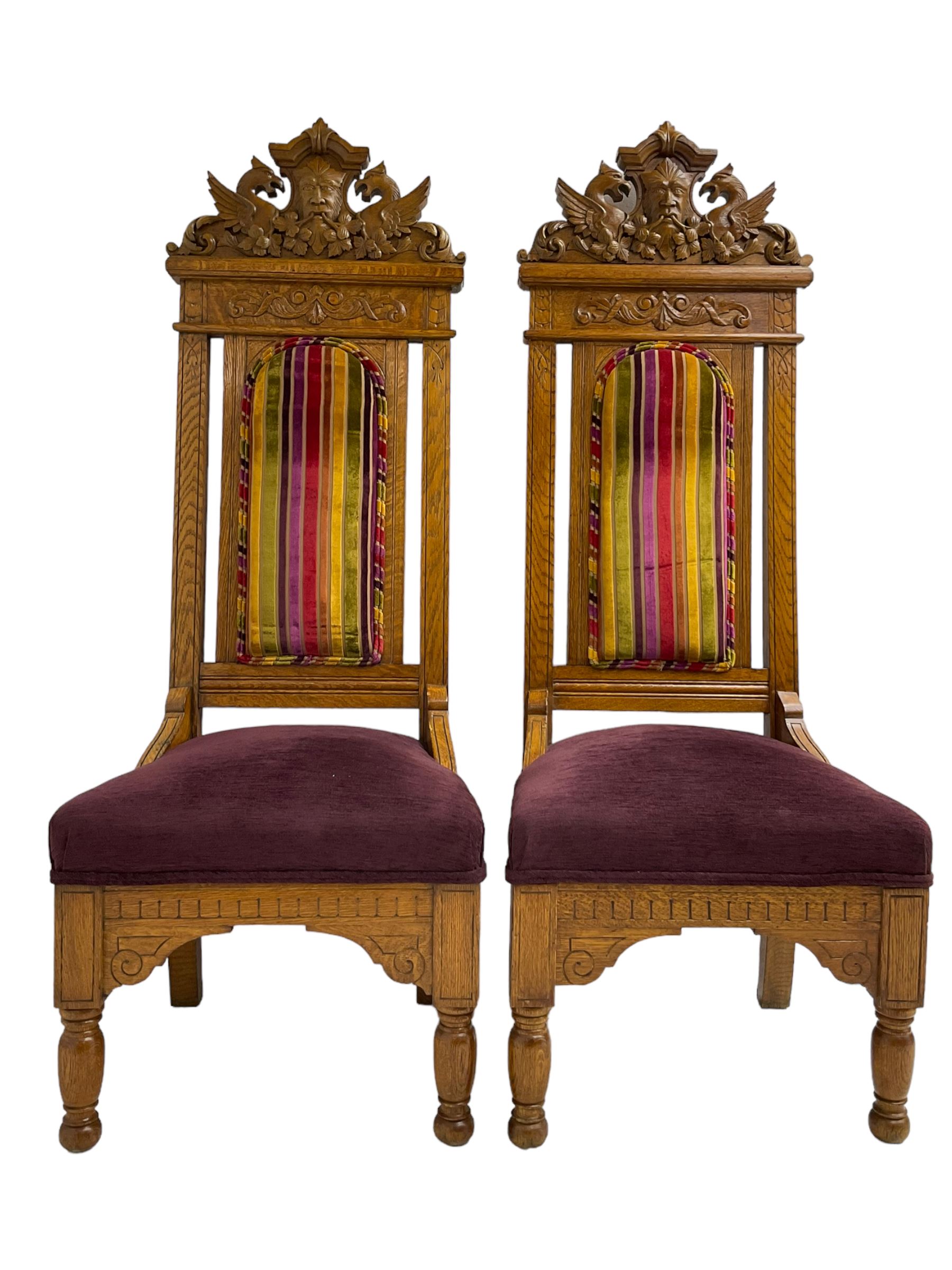 Set of six 20th century Carolean design oak high back chairs, the pediment carved with dragons and central Green Man mask with trailing foliage, the backs upholstered in striped fabric, on turned front supports