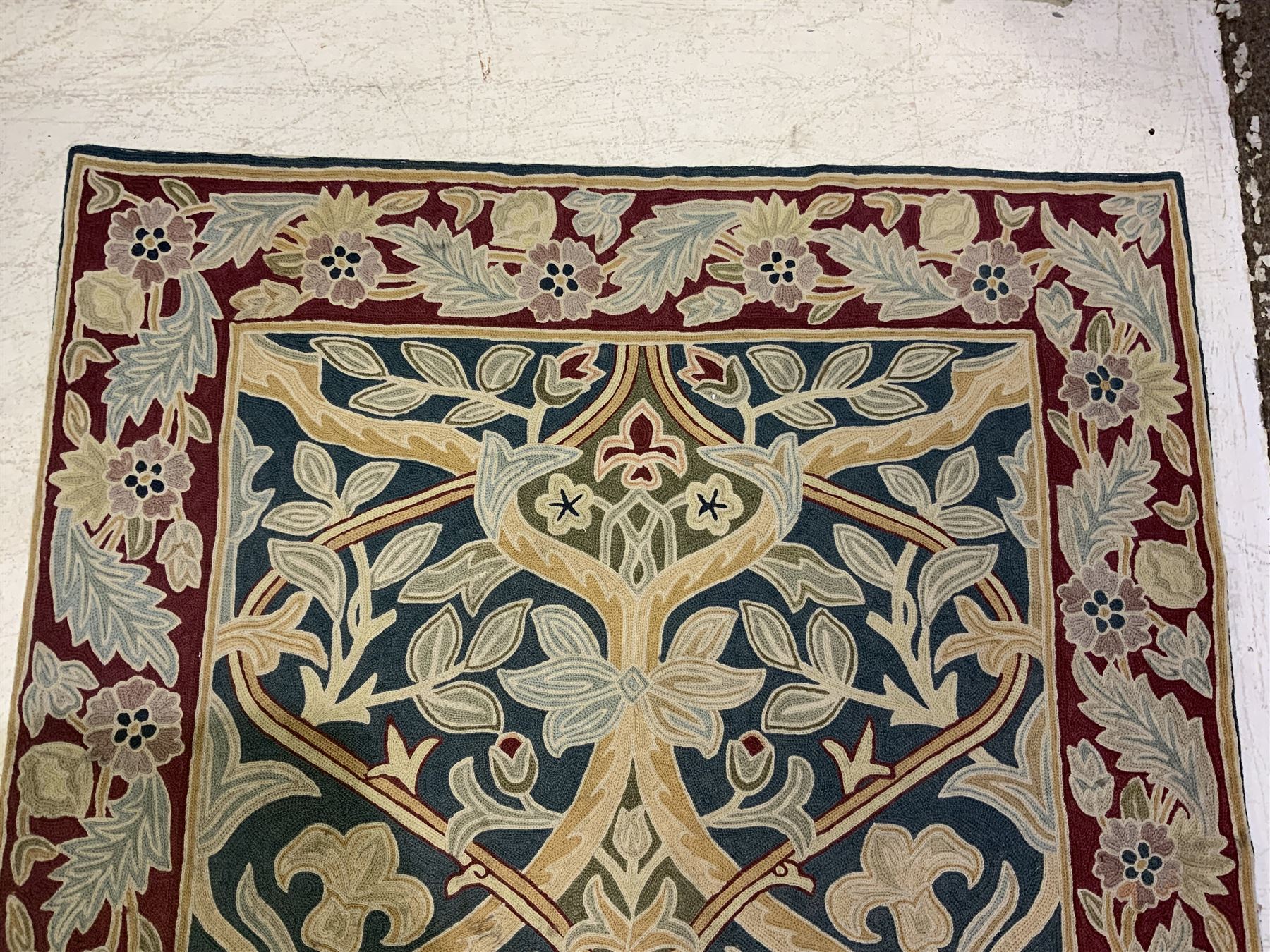 Caucasian design crewelwork hanging, the field decorated with a stylised tree of life motifs with surrounding leafage, enclosed by a crimson ground border with foliate designs