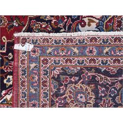 Large Kashan crimson ground carpet, central indigo medallion with stylised floral motifs, flanked by matching spandrels, bordered by multiple bands featuring repeating foliate and floral designs throughout