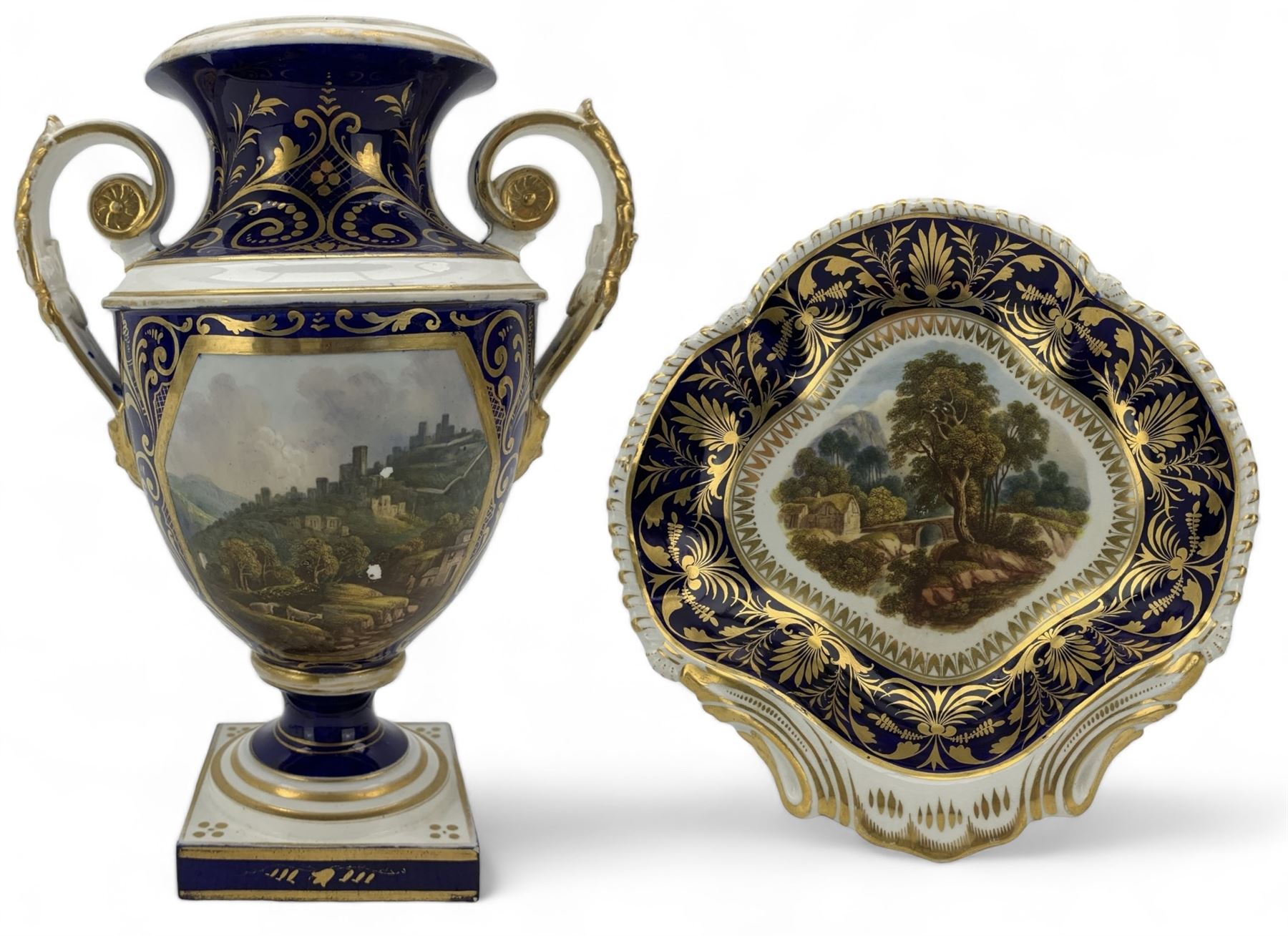 Early 19th century Derby porcelain urn, the reserve painted with a pastoral landscape and castle in the distance, with twin scroll and mask handles, upon a square pedestal base, H23cm, together with a Derby shell-shaped dish, centrally hand painted with a landscape scene titled 'In North Wales', within a cobalt blue and gilt border, L25cm (2)