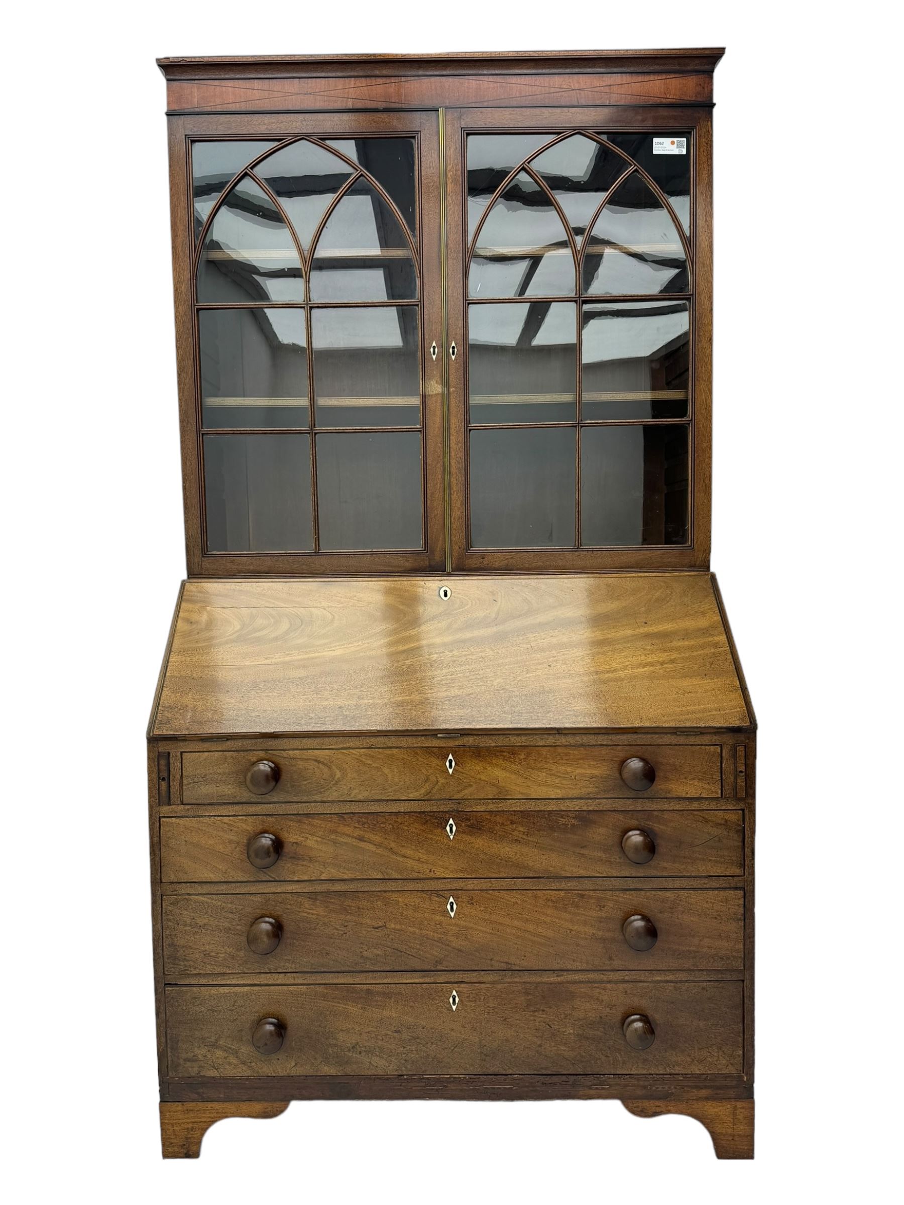 Early 19th century mahogany bureau bookcase, the projecting cornice over two Gothic-style astragal glazed doors enclosing two adjustable shelves, sloped hinged lid enclosing fitted interior and felt inset, four graduating drawers, on bracket feet