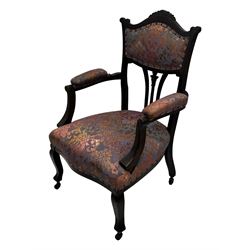 Late Victorian mahogany framed armchair, upholstered in muted purple fabric with iridescent floral pattern and nailhead trim, central foliate carved splat over padded scrolled arms, on cabriole supports fitted with castors