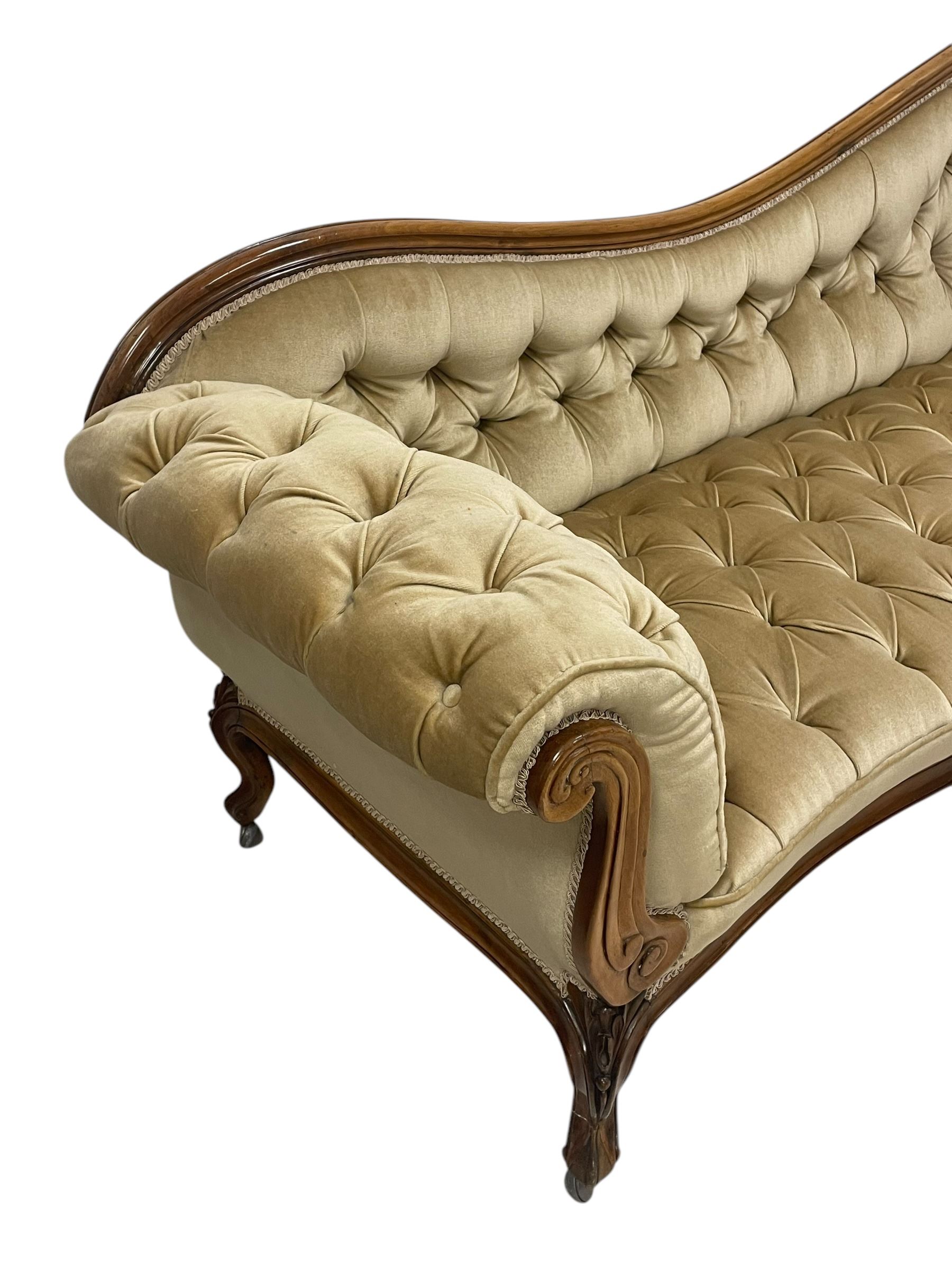 19th century walnut framed chaise longue, shaped back over scrolled arms decorated with moulded curling acanthus carvings, upholstered in deep buttoned champagne fabric, raised on cabriole supports with applied floral carved decoration, on castors