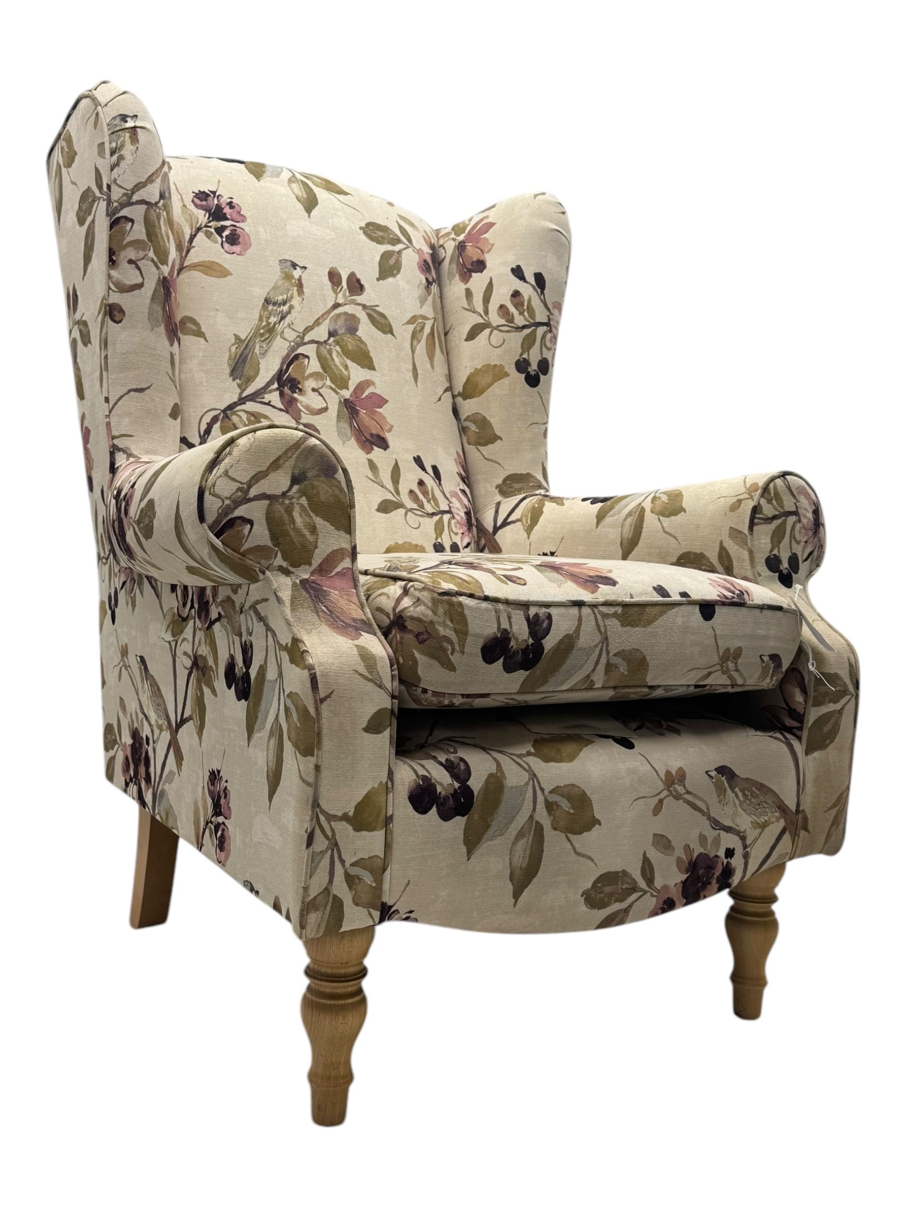 Hardwood-framed wingback armchair, upholstered in cream floral pattern fabric, on turned front feet