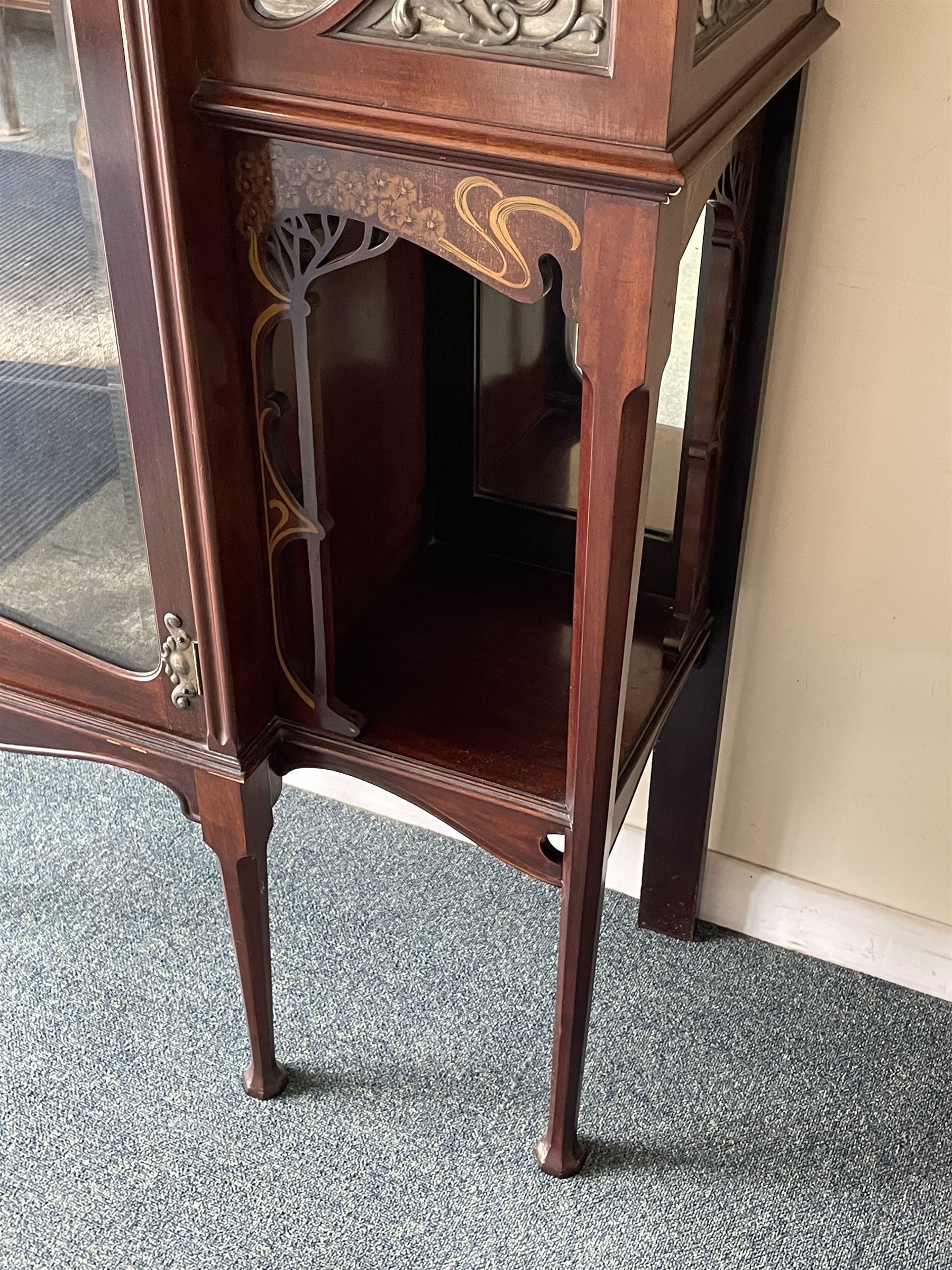 Art Nouveau period inlaid mahogany display cabinet, raised shaped and moulded pediment over projecting moulded cornices, the upper frieze inlaid with trailing branches and tulips, single astragal and bevel glazed door enclosed velvet lined interior fitted with shelves, flanked by curved glass panes decorated with pierced metal foliate spandrels, lower flanking shelves with mirror backs enclosed within shaped and pierced rails inlaid with flower heads, on tapering octagonal supports terminating to compressed pad feet, the lock stamped 'Salmon Bros, London' 